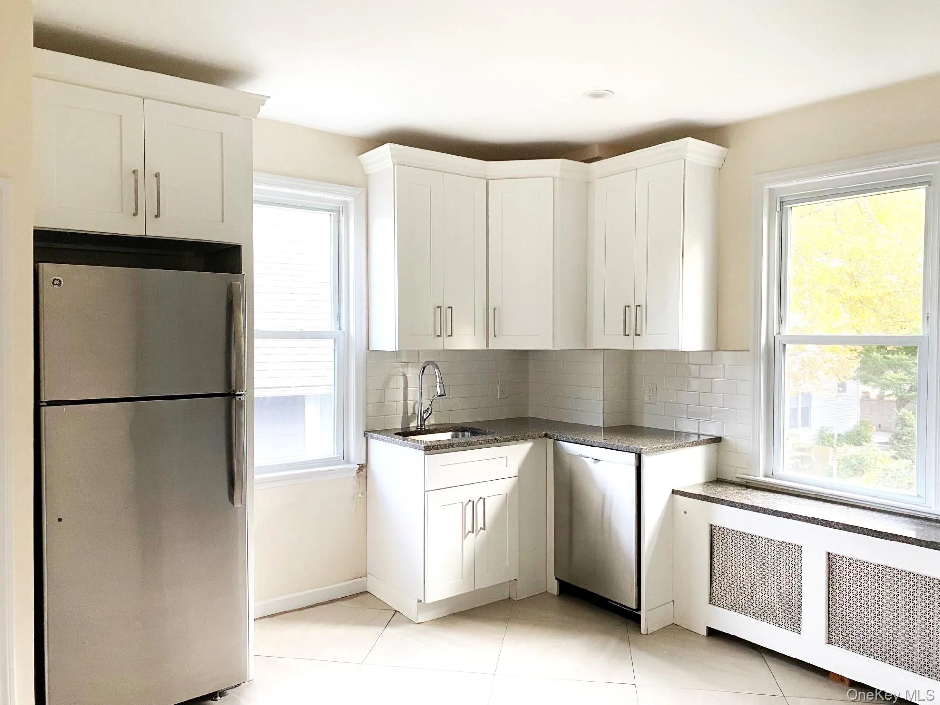 Kitchen featuring stainless steel appliances, white cabinets, radiator heating unit, dark stone countertops, and decorative backsplash Kitchen featuring stainless steel appliances, white cabinets, radiator heating unit, dark stone countertops, and decorative backsplash