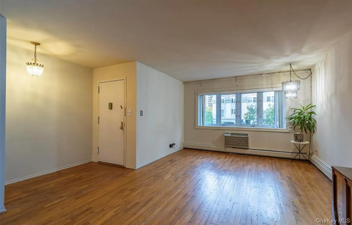 Unfurnished room with a chandelier, wood-type flooring, a wall mounted AC, and baseboard heating Unfurnished room with a chandelier, wood-type flooring, a wall mounted AC, and baseboard heating