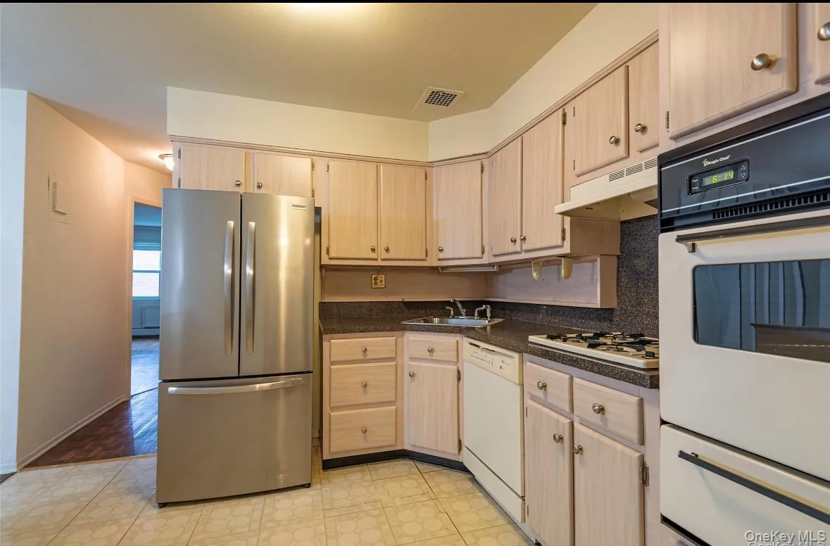 Kitchen with white appliances, light brown cabinets, dark countertops, and a warming drawer Kitchen with white appliances, light brown cabinets, dark countertops, and a warming drawer