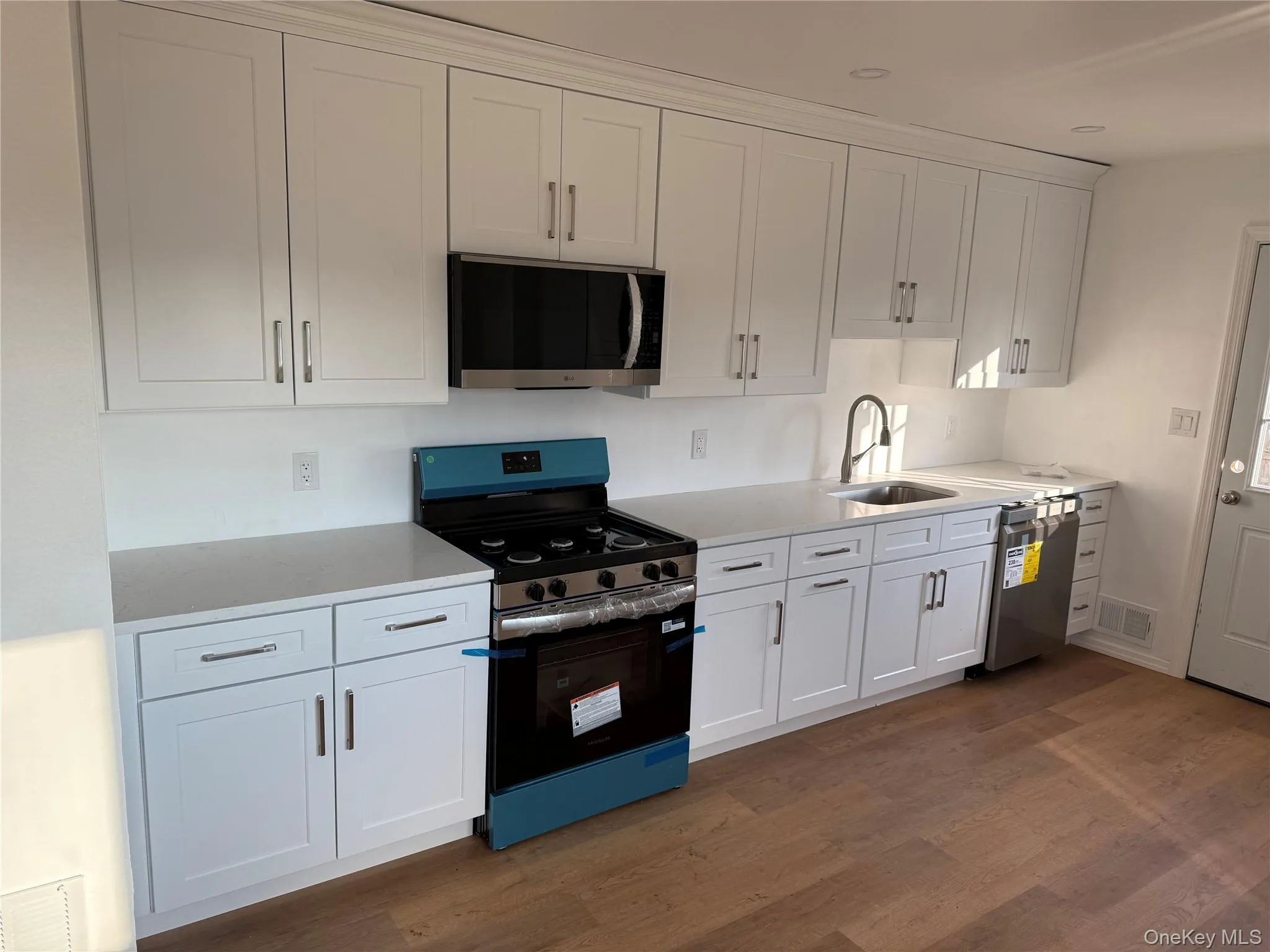 Kitchen with stainless steel appliances, white cabinetry, light stone countertops, and dark wood-style floors Kitchen with stainless steel appliances, white cabinetry, light stone countertops, and dark wood-style floors