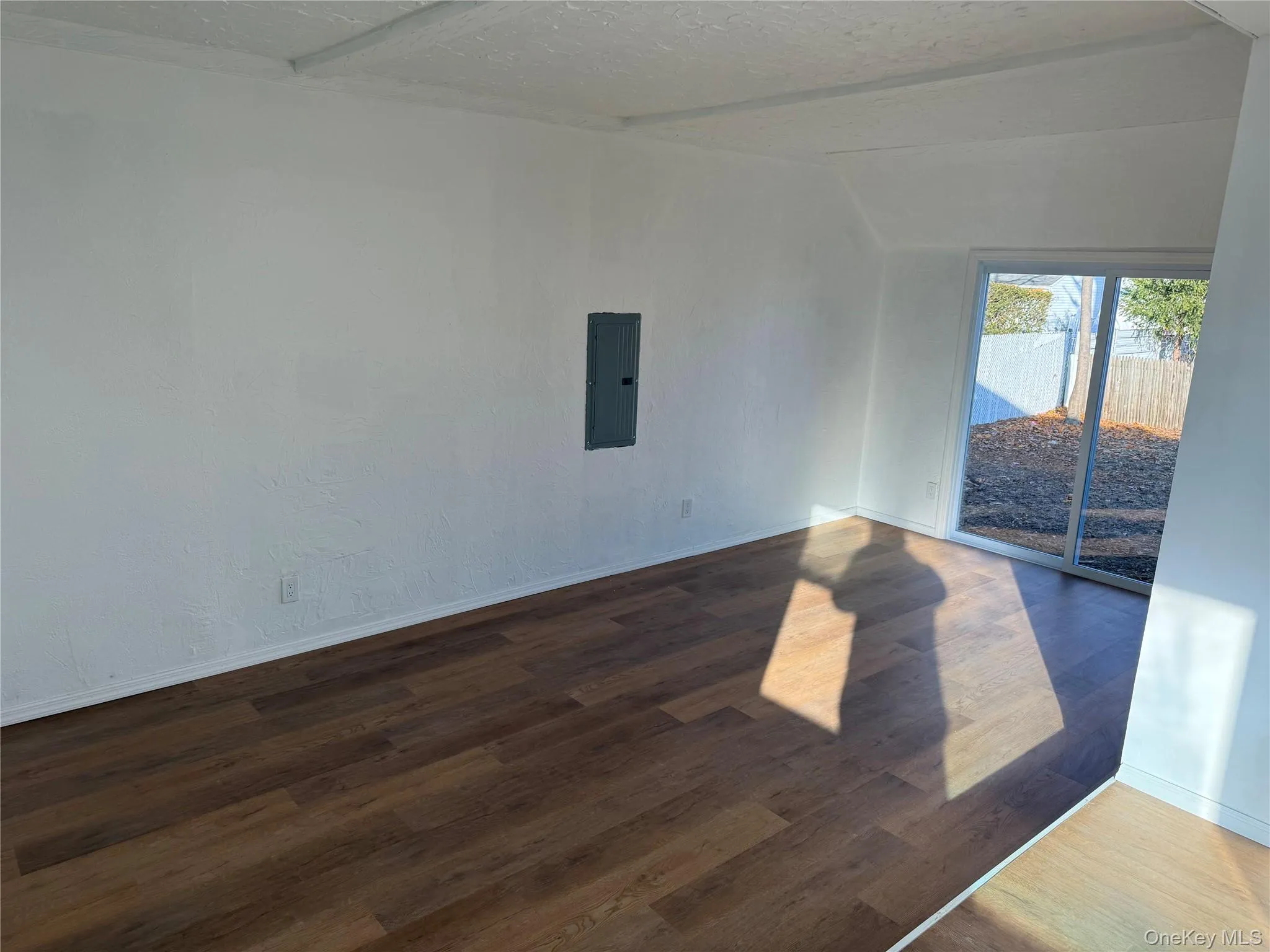 Unfurnished room with a textured ceiling, wood finished floors, electric panel, and vaulted ceiling Unfurnished room with a textured ceiling, wood finished floors, electric panel, and vaulted ceiling