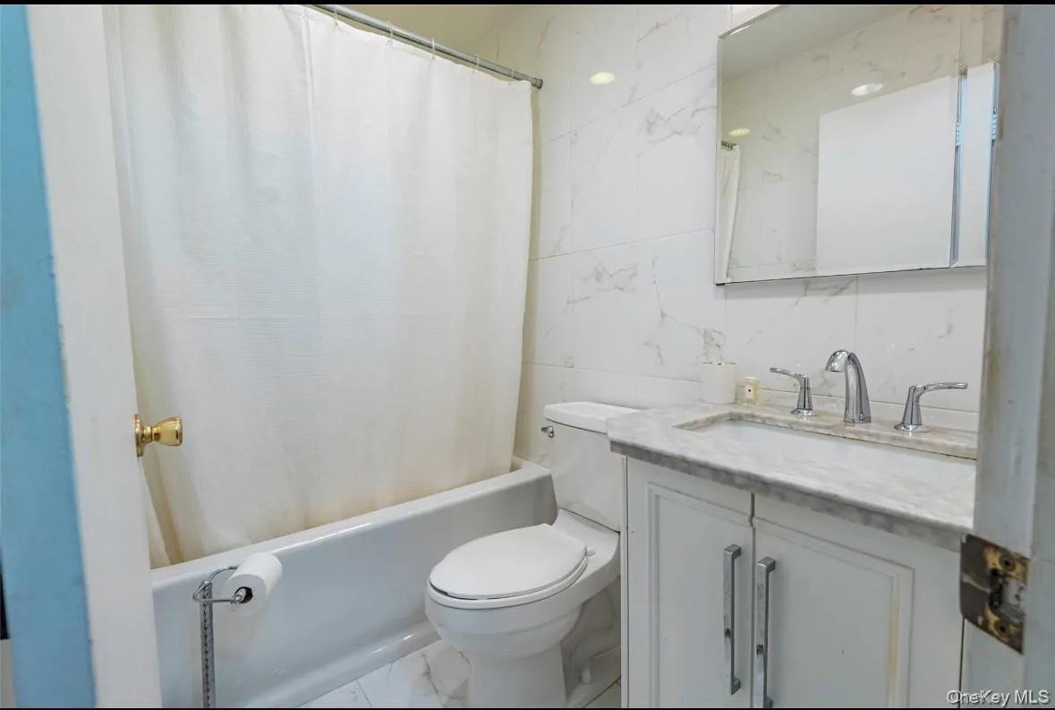 Full bath with tile walls, marble look tile flooring, vanity, and shower / tub combo Full bath with tile walls, marble look tile flooring, vanity, and shower / tub combo