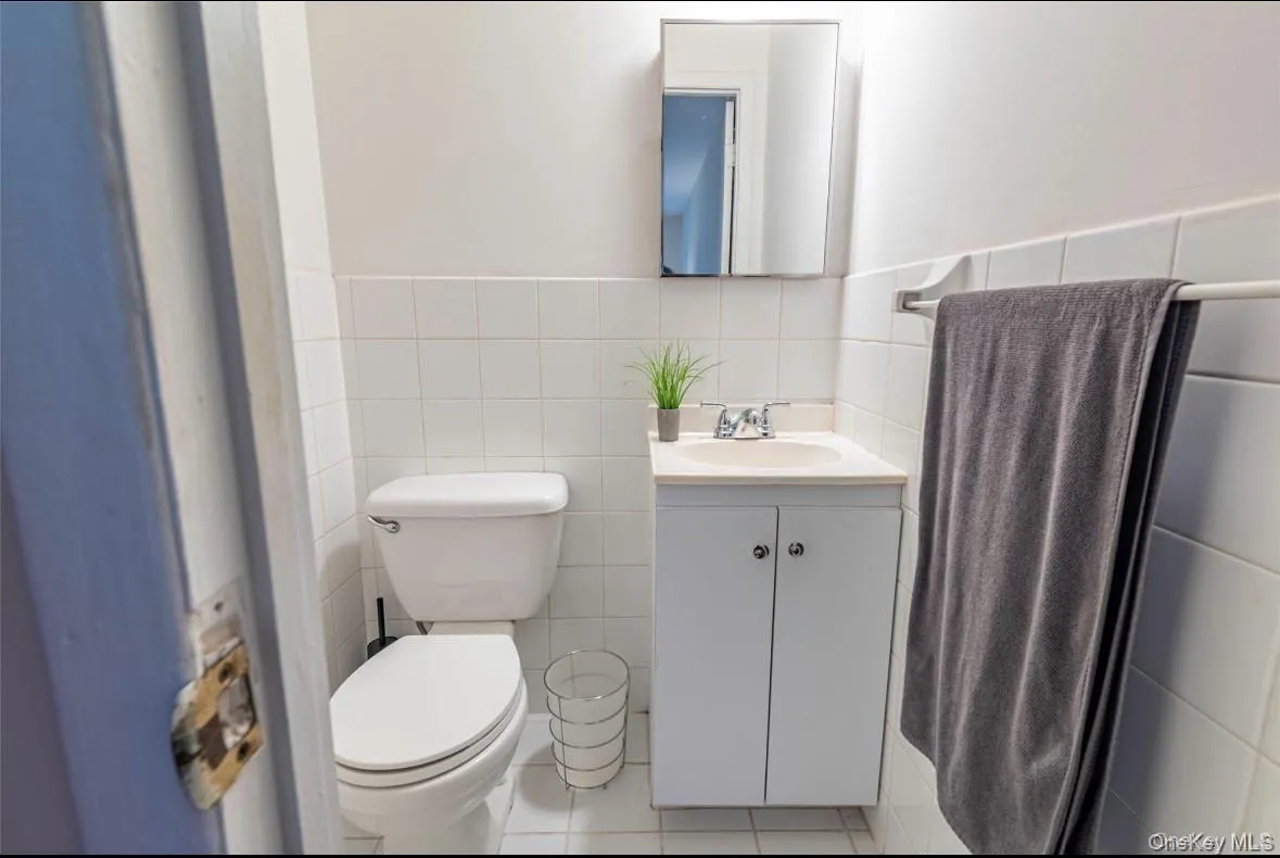 Half bath featuring tile walls, vanity, a wainscoted wall, and tile patterned floors Half bath featuring tile walls, vanity, a wainscoted wall, and tile patterned floors