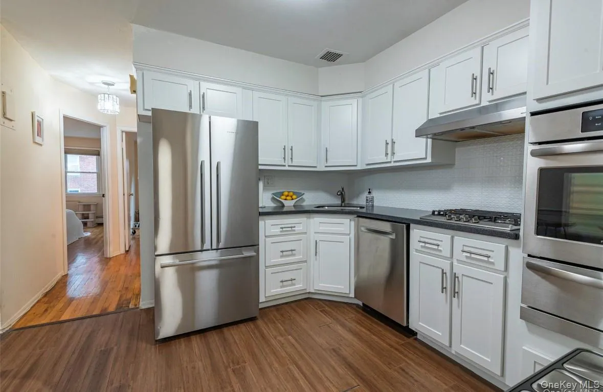 Kitchen featuring appliances with stainless steel finishes, white cabinets, a warming drawer, and dark wood finished floors Kitchen featuring appliances with stainless steel finishes, white cabinets, a warming drawer, and dark wood finished floors