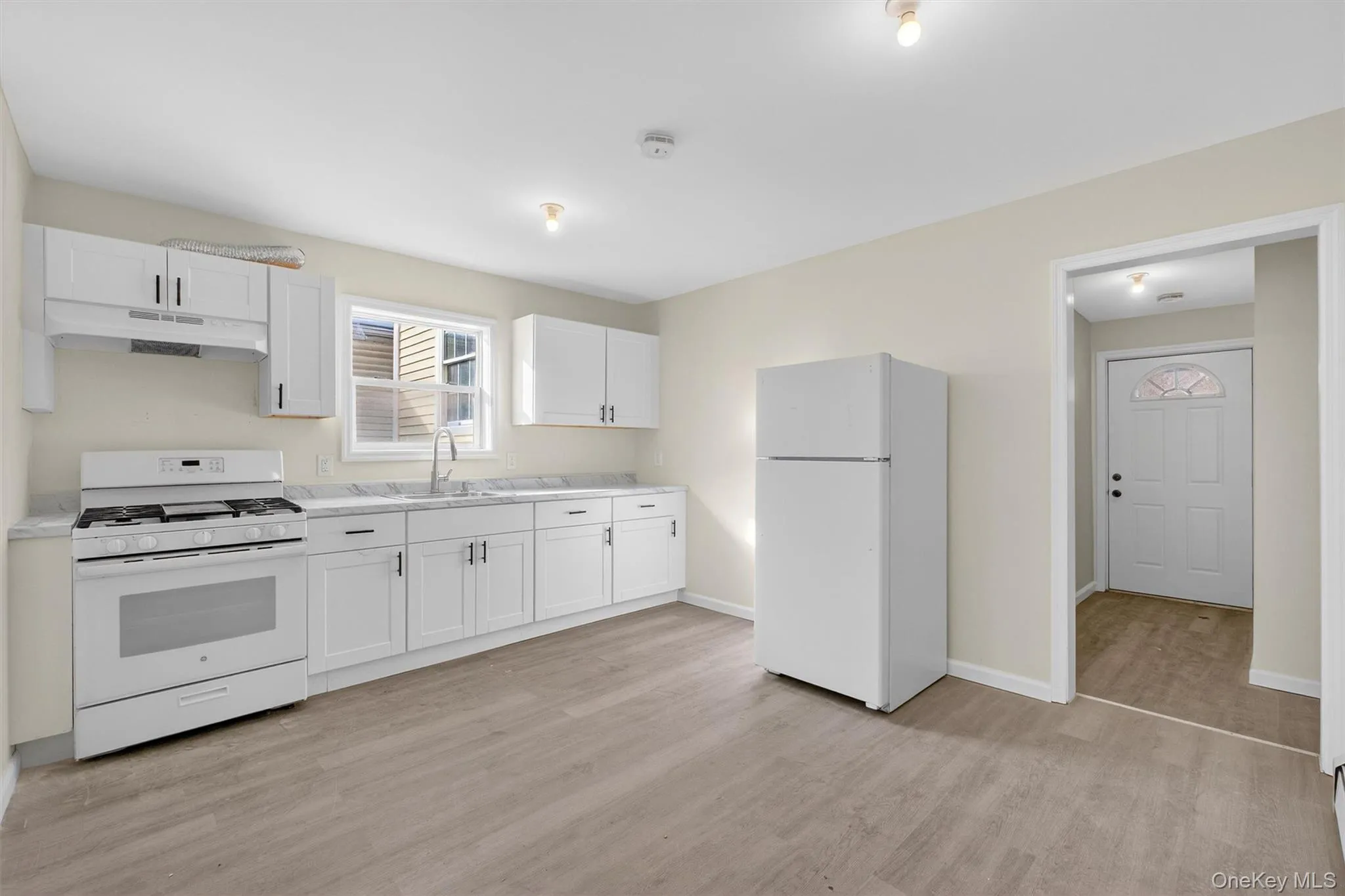 Kitchen featuring white appliances, light countertops, white cabinetry, under cabinet range hood, and light wood-style floors Kitchen featuring white appliances, light countertops, white cabinetry, under cabinet range hood, and light wood-style floors
