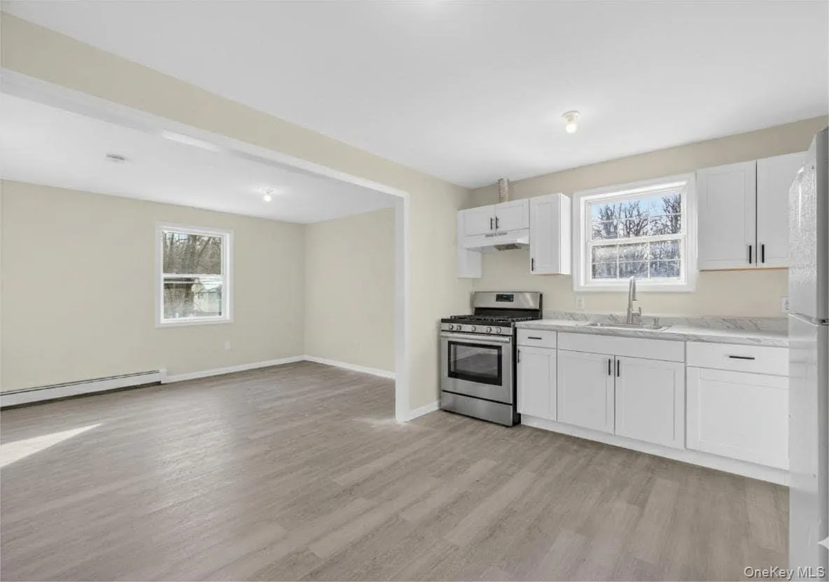 Kitchen featuring gas range, white cabinetry, light wood-style flooring, light countertops, and a baseboard heating unit Kitchen featuring gas range, white cabinetry, light wood-style flooring, light countertops, and a baseboard heating unit