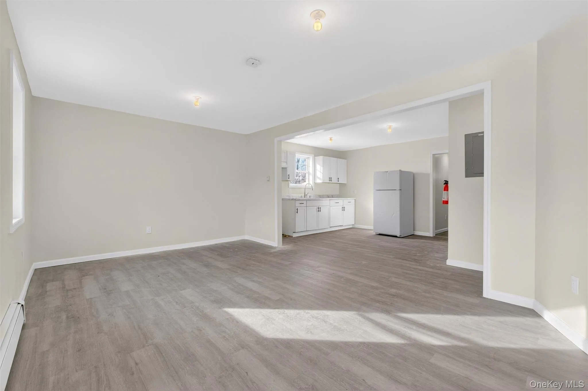 Unfurnished living room with light wood finished floors, baseboard heating, and electric panel Unfurnished living room with light wood finished floors, baseboard heating, and electric panel