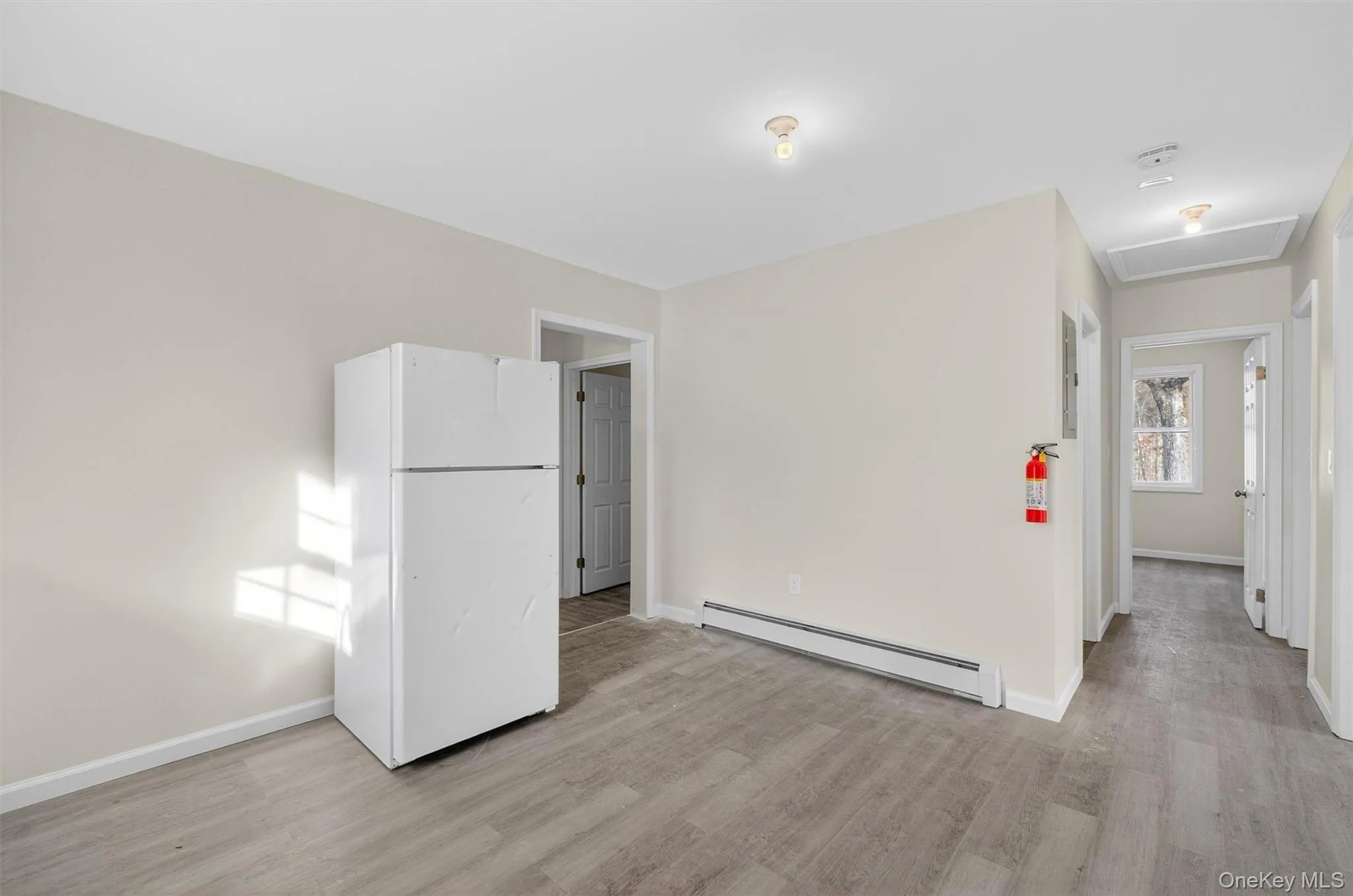 Spare room with baseboard heating, attic access, and light wood-style flooring Spare room with baseboard heating, attic access, and light wood-style flooring