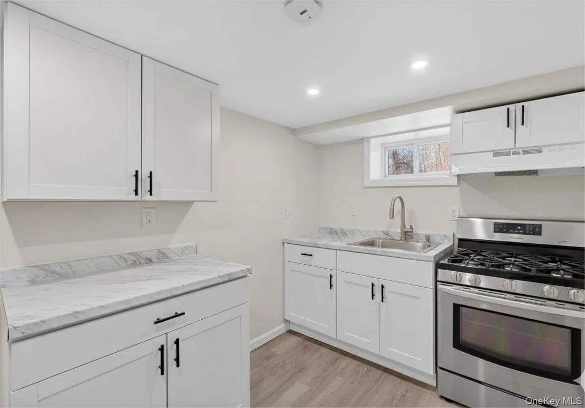 Kitchen with stainless steel gas stove, light countertops, white cabinets, under cabinet range hood, and recessed lighting Kitchen with stainless steel gas stove, light countertops, white cabinets, under cabinet range hood, and recessed lighting