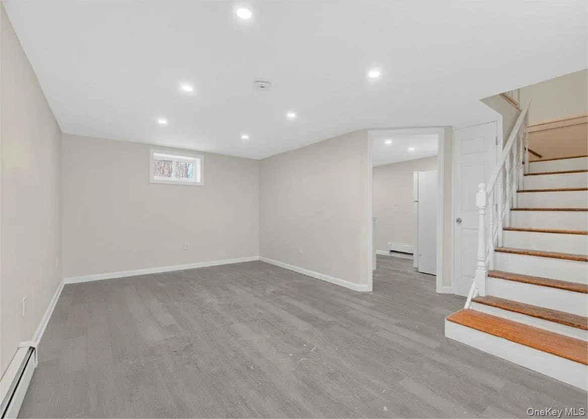 Below grade area featuring baseboard heating, stairs, recessed lighting, freestanding refrigerator, and a baseboard heating unit Below grade area featuring baseboard heating, stairs, recessed lighting, freestanding refrigerator, and a baseboard heating unit