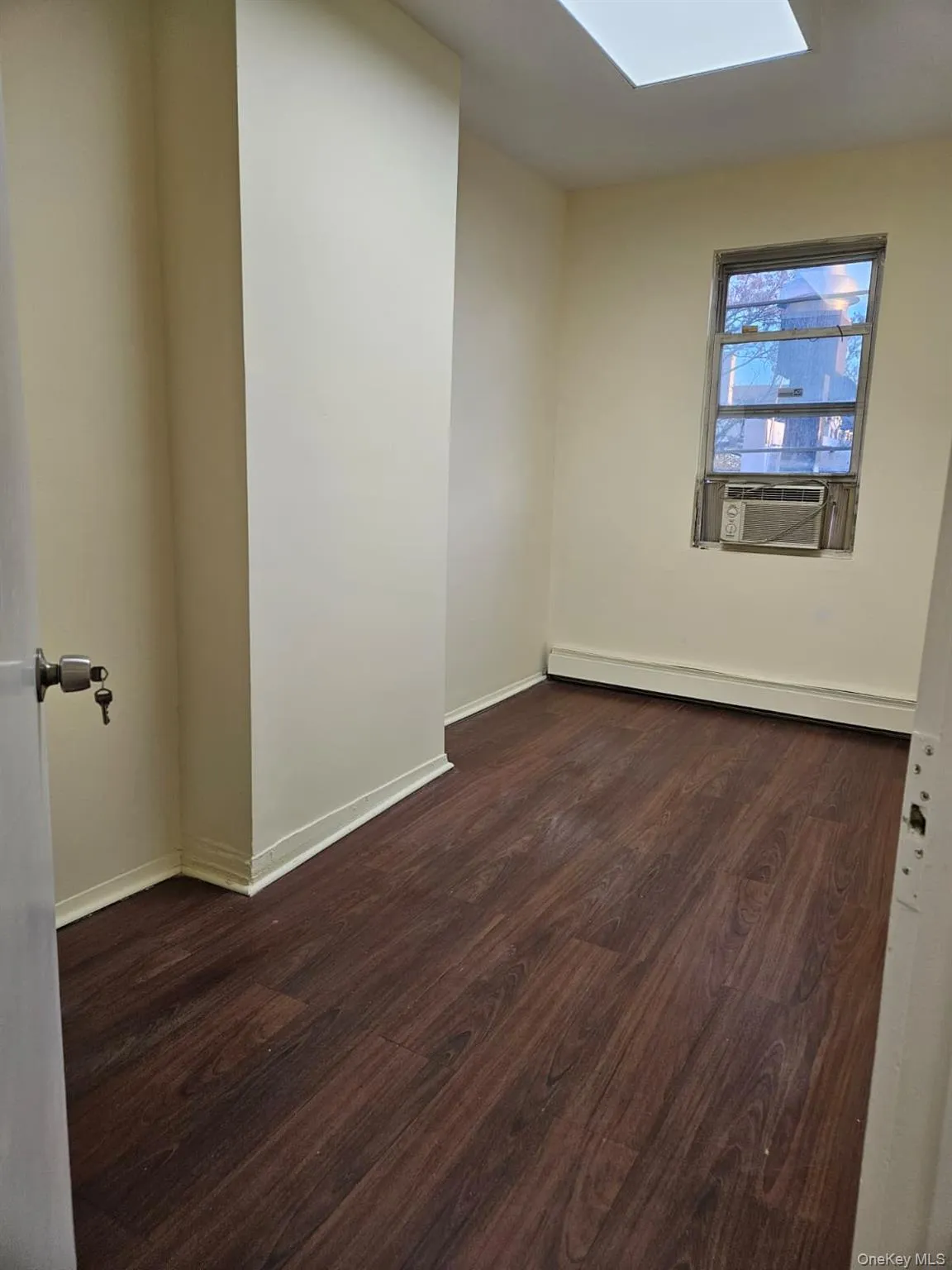 Unfurnished room featuring dark wood-style floors, a baseboard heating unit, a skylight, and cooling unit Unfurnished room featuring dark wood-style floors, a baseboard heating unit, a skylight, and cooling unit