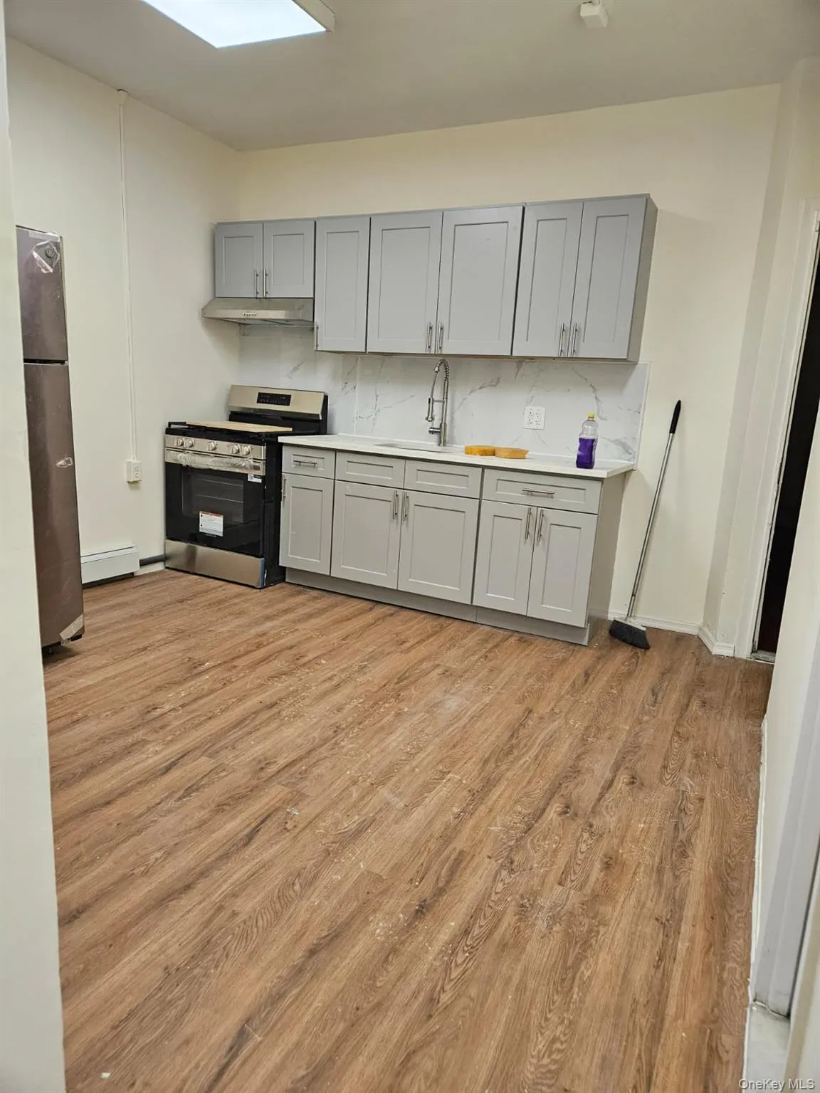 Kitchen with gray cabinets, stainless steel appliances, light wood-style floors, tasteful backsplash, and a skylight Kitchen with gray cabinets, stainless steel appliances, light wood-style floors, tasteful backsplash, and a skylight