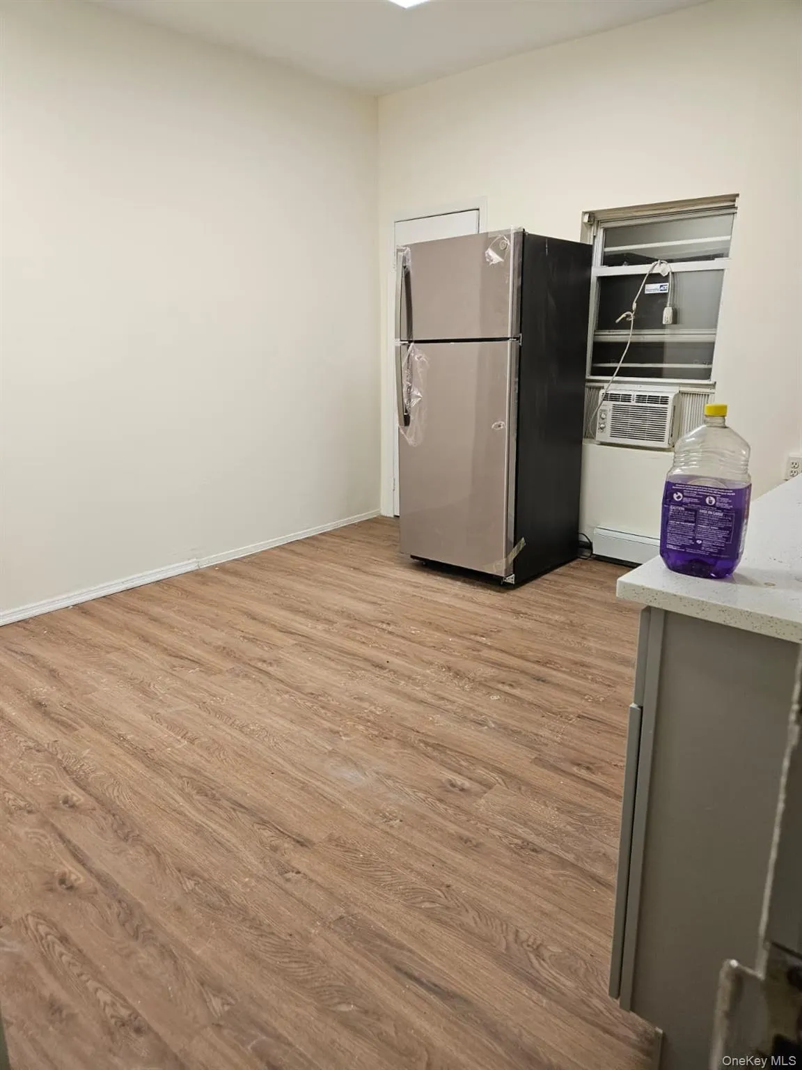 Kitchen with freestanding refrigerator, light wood finished floors, light stone countertops, cooling unit, and gray cabinets Kitchen with freestanding refrigerator, light wood finished floors, light stone countertops, cooling unit, and gray cabinets