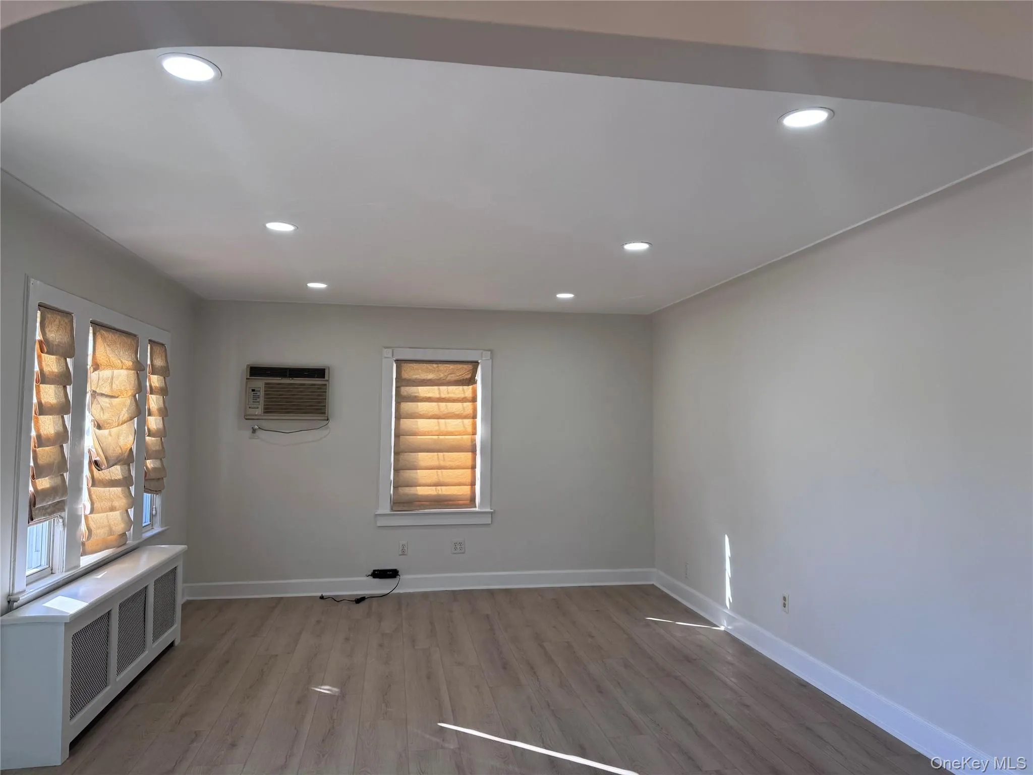 Empty room with radiator heating unit, recessed lighting, wood finished floors, and an AC wall unit Empty room with radiator heating unit, recessed lighting, wood finished floors, and an AC wall unit