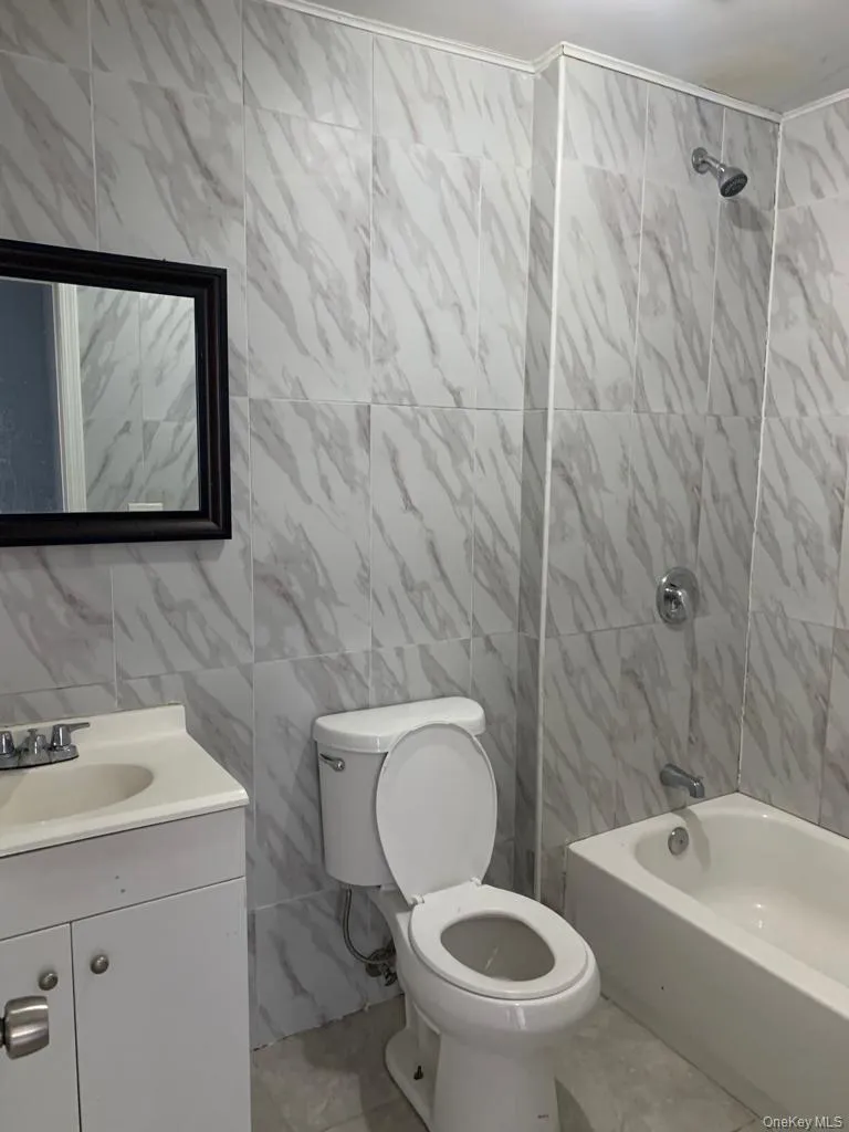 Full bath featuring tile walls, bathing tub / shower combination, vanity, and light marble finish floors Full bath featuring tile walls, bathing tub / shower combination, vanity, and light marble finish floors
