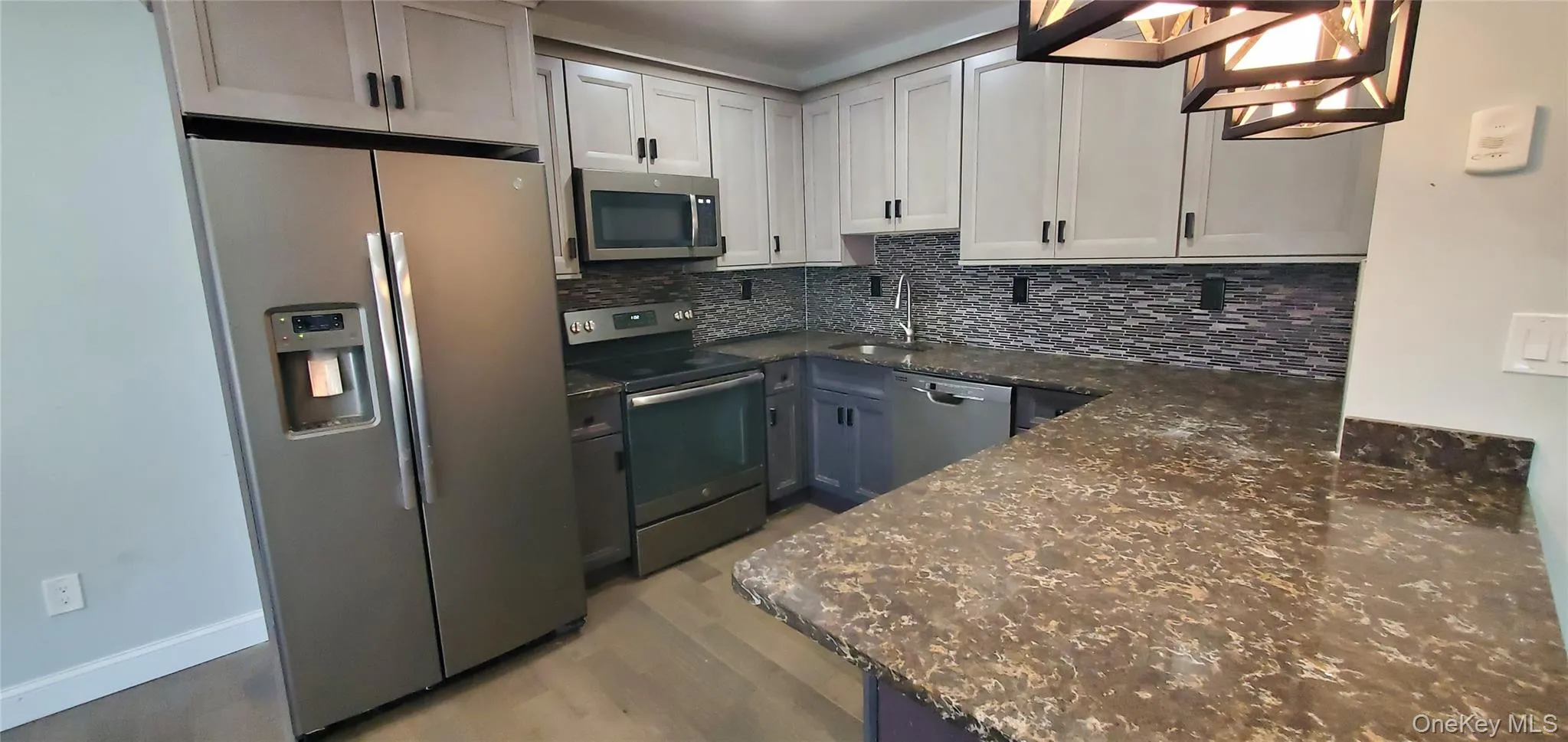 Kitchen featuring dark stone countertops, stainless steel appliances, light wood-style floors, decorative backsplash, and pendant lighting Kitchen featuring dark stone countertops, stainless steel appliances, light wood-style floors, decorative backsplash, and pendant lighting