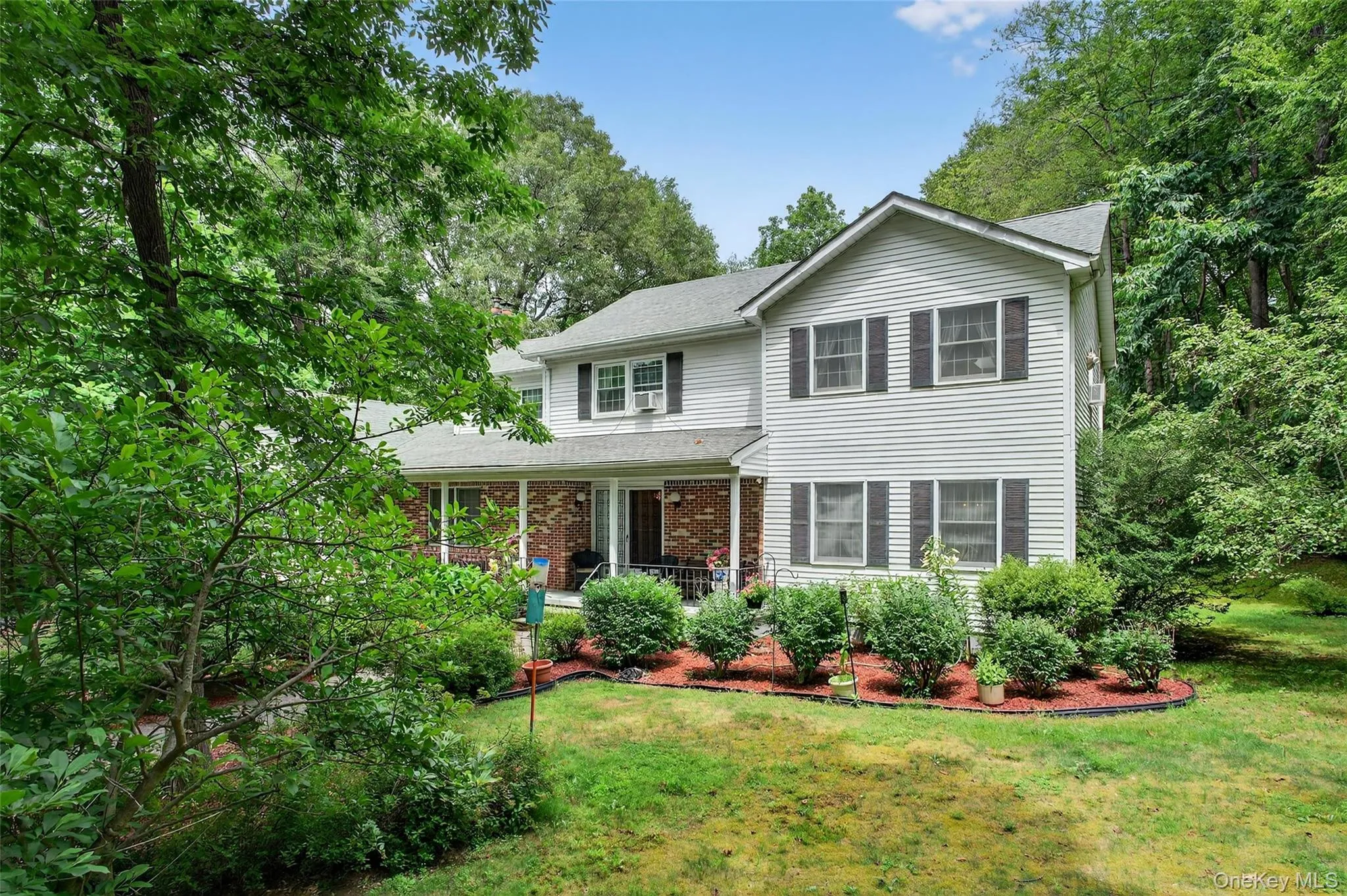 View of front of property featuring brick siding, a front lawn, view of wooded area, and roof with shingles View of front of property featuring brick siding, a front lawn, view of wooded area, and roof with shingles