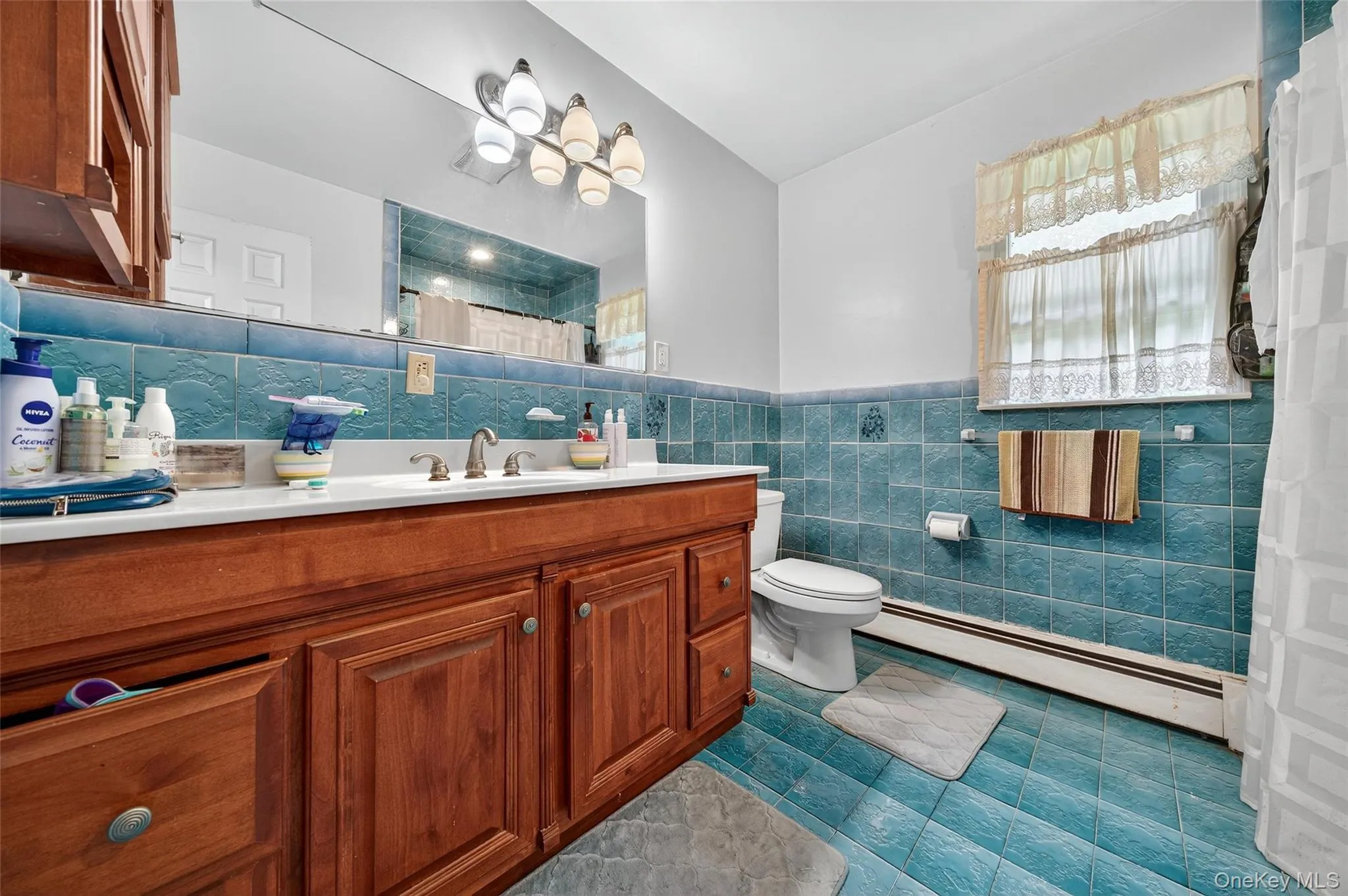 Full bath with a baseboard heating unit, vanity, tile patterned flooring, wainscoting, and tile walls Full bath with a baseboard heating unit, vanity, tile patterned flooring, wainscoting, and tile walls