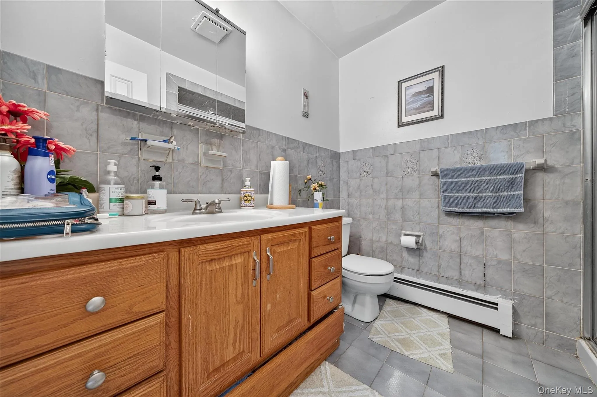 Full bath featuring tile walls, a baseboard radiator, vanity, light tile patterned flooring, and a shower with shower door Full bath featuring tile walls, a baseboard radiator, vanity, light tile patterned flooring, and a shower with shower door