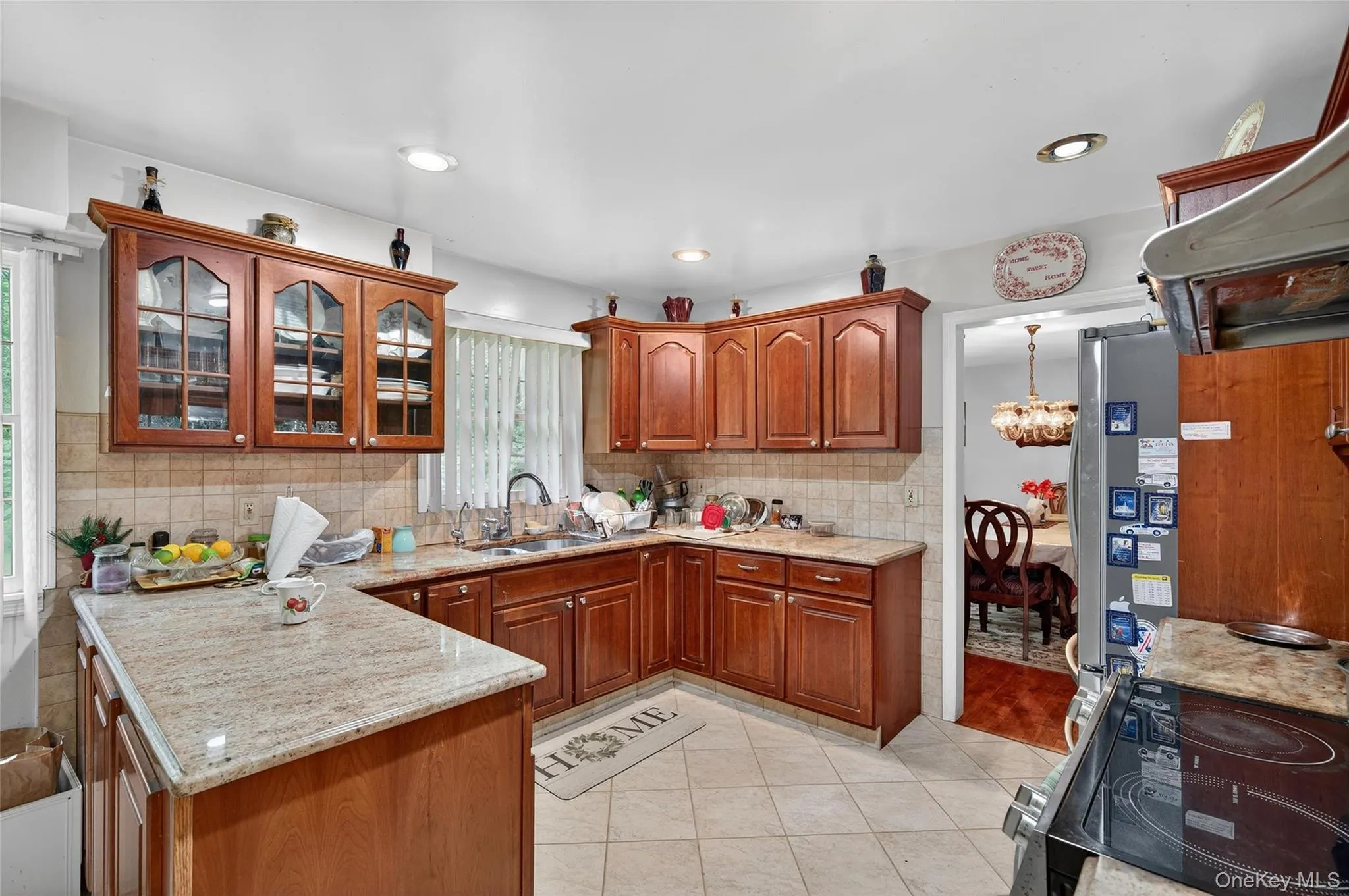 Kitchen featuring brown cabinetry, range with electric stovetop, glass insert cabinets, freestanding refrigerator, and recessed lighting Kitchen featuring brown cabinetry, range with electric stovetop, glass insert cabinets, freestanding refrigerator, and recessed lighting