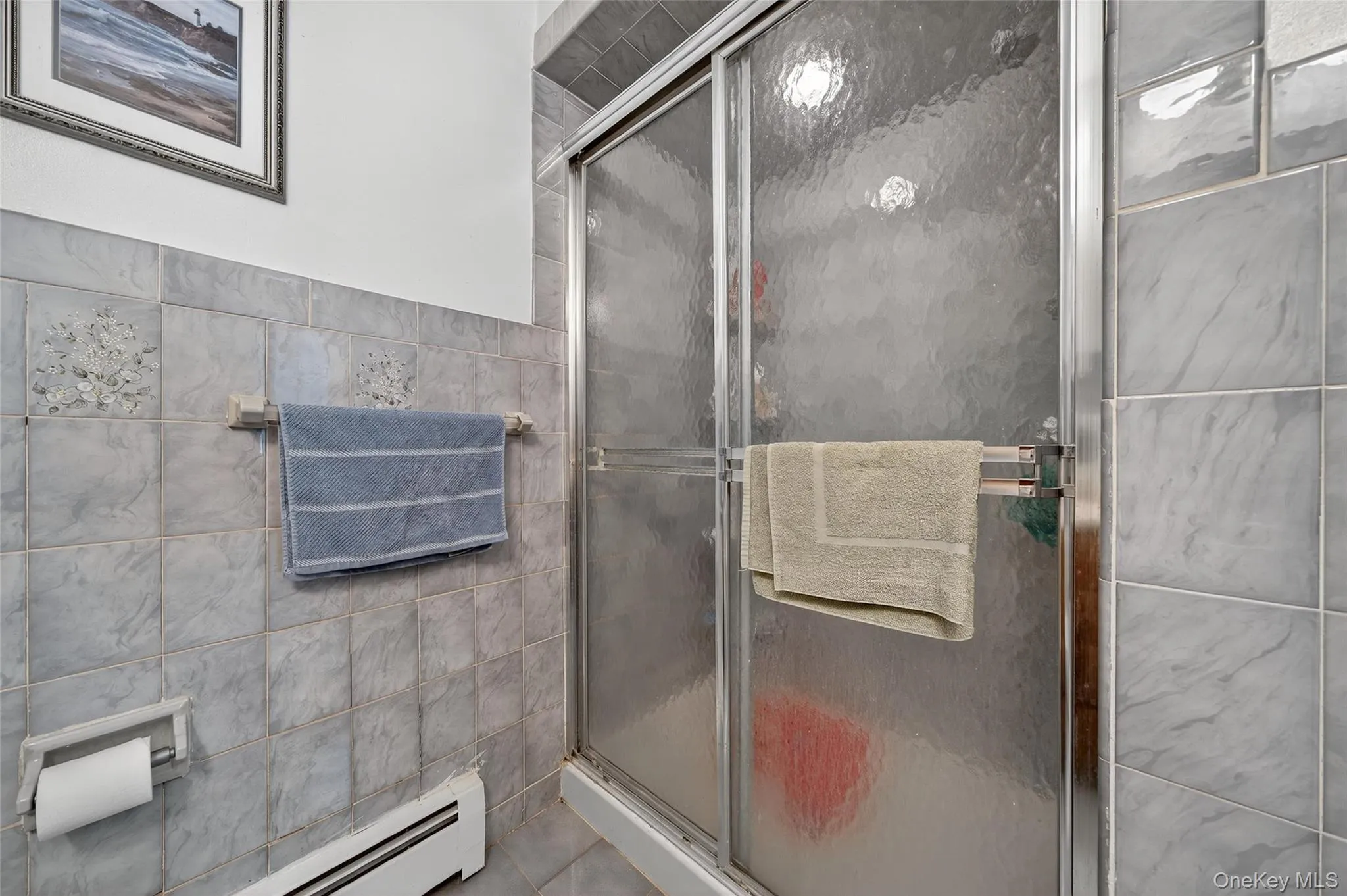 Full bathroom featuring tile walls, a stall shower, a baseboard heating unit, and tile patterned flooring Full bathroom featuring tile walls, a stall shower, a baseboard heating unit, and tile patterned flooring