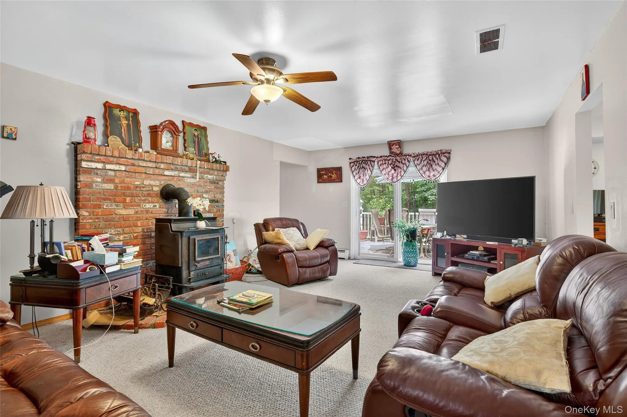 Living room with a wood stove, carpet floors, and ceiling fan Living room with a wood stove, carpet floors, and ceiling fan