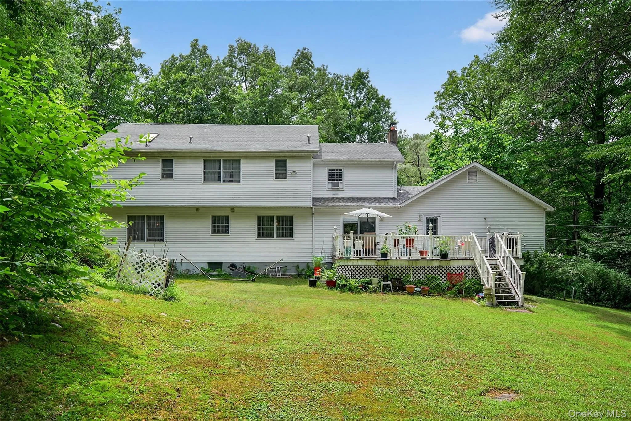 Back of house featuring a chimney, a wooden deck, stairs, a yard, and view of wooded area Back of house featuring a chimney, a wooden deck, stairs, a yard, and view of wooded area