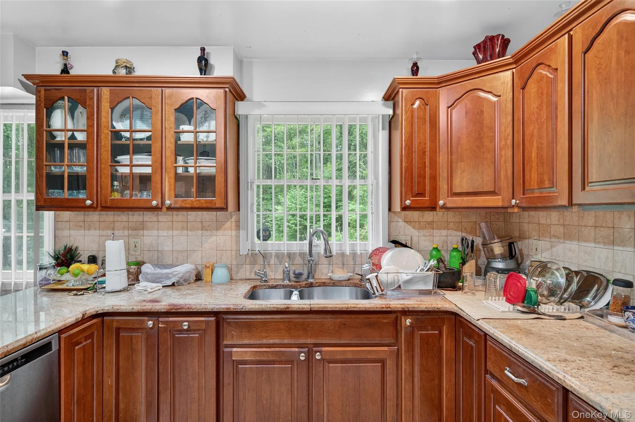 Kitchen featuring decorative backsplash, dishwasher, brown cabinetry, and light stone counters Kitchen featuring decorative backsplash, dishwasher, brown cabinetry, and light stone counters