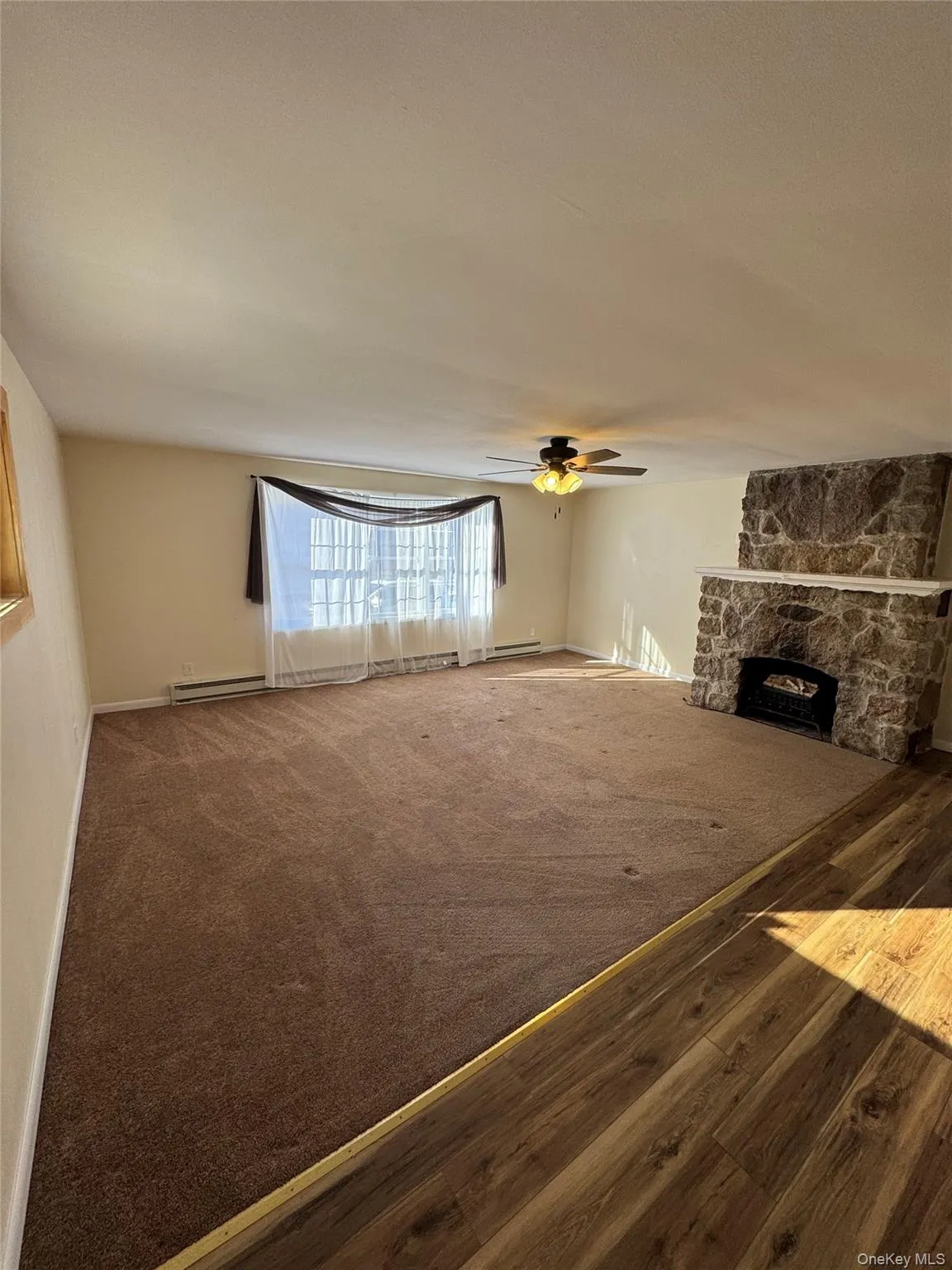 Unfurnished living room featuring a fireplace, a baseboard heating unit, carpet flooring, and a ceiling fan Unfurnished living room featuring a fireplace, a baseboard heating unit, carpet flooring, and a ceiling fan