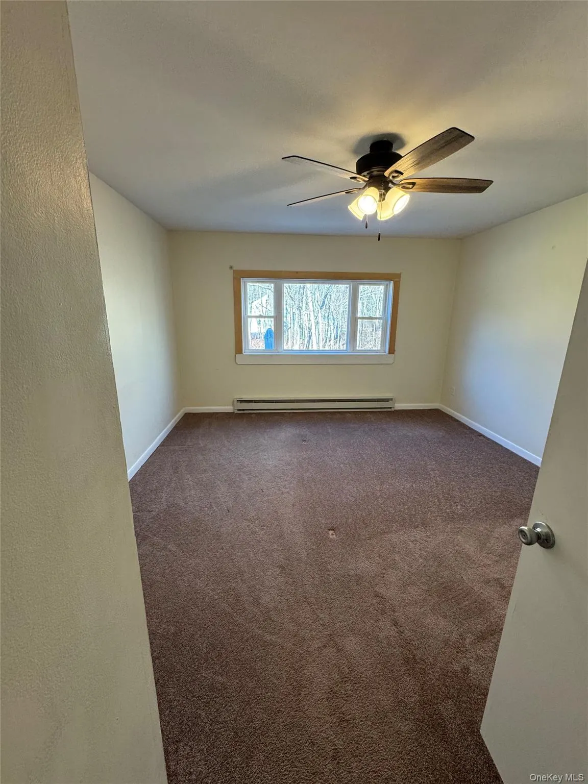 Empty room with dark colored carpet, baseboard heating, and ceiling fan Empty room with dark colored carpet, baseboard heating, and ceiling fan