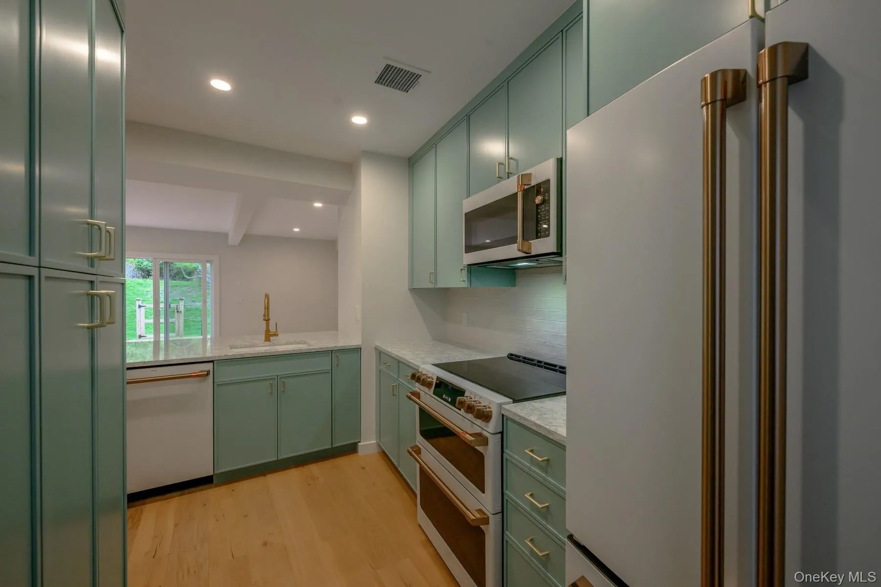 Kitchen with green cabinetry, white appliances, light stone counters, light wood-style flooring, and recessed lighting Kitchen with green cabinetry, white appliances, light stone counters, light wood-style flooring, and recessed lighting