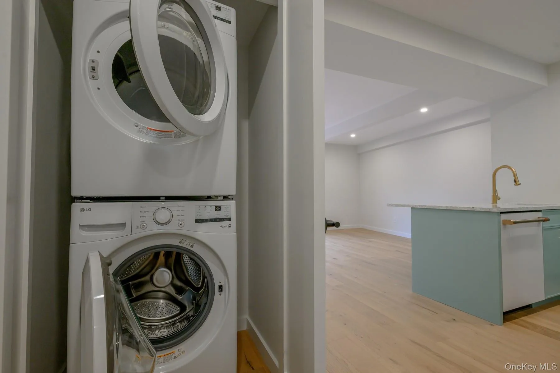 Washroom with light wood-style flooring, stacked washing machine and dryer, and recessed lighting Washroom with light wood-style flooring, stacked washing machine and dryer, and recessed lighting