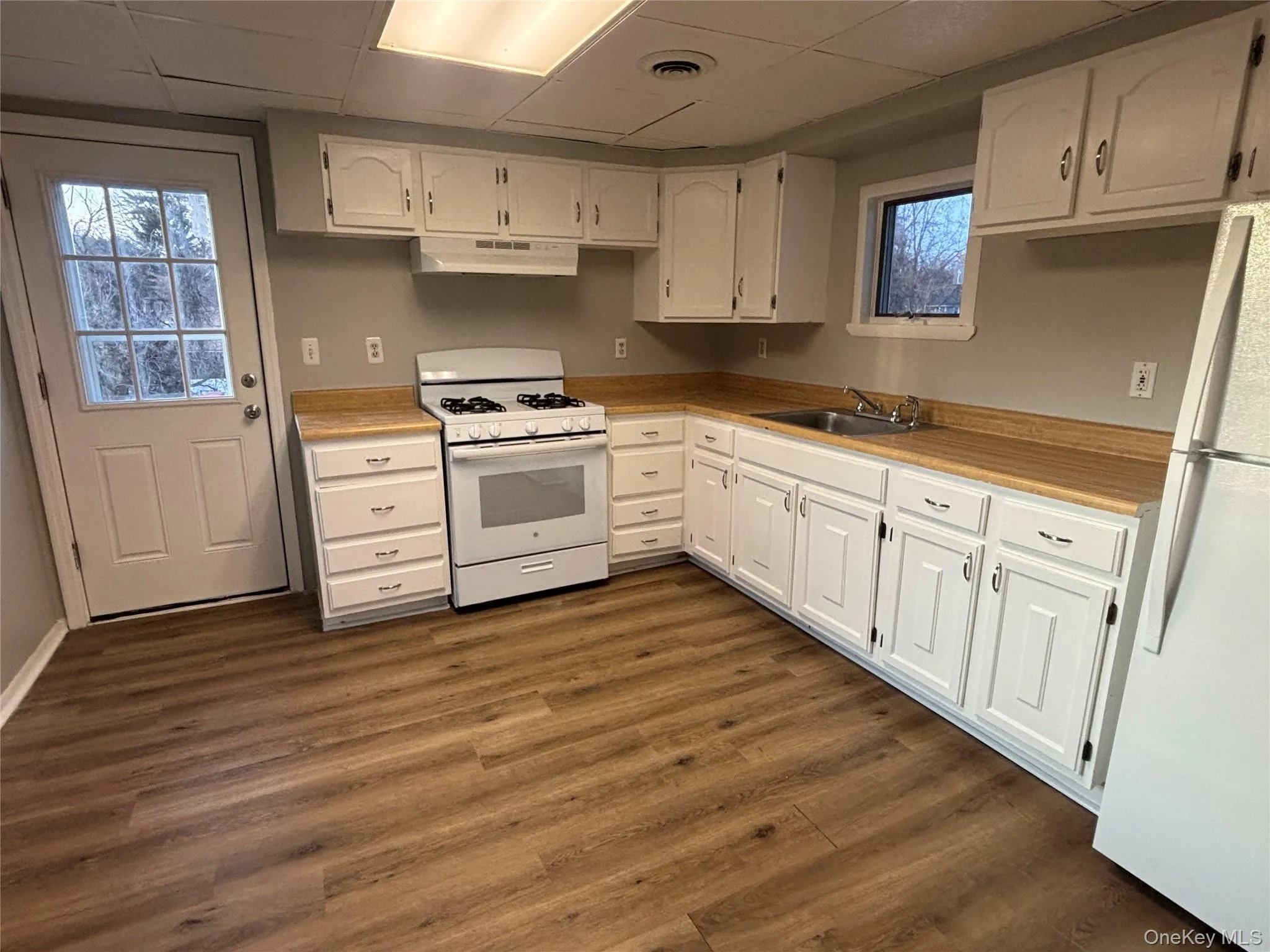 Kitchen featuring white appliances, light countertops, a paneled ceiling, white cabinetry, and dark wood finished floors Kitchen featuring white appliances, light countertops, a paneled ceiling, white cabinetry, and dark wood finished floors