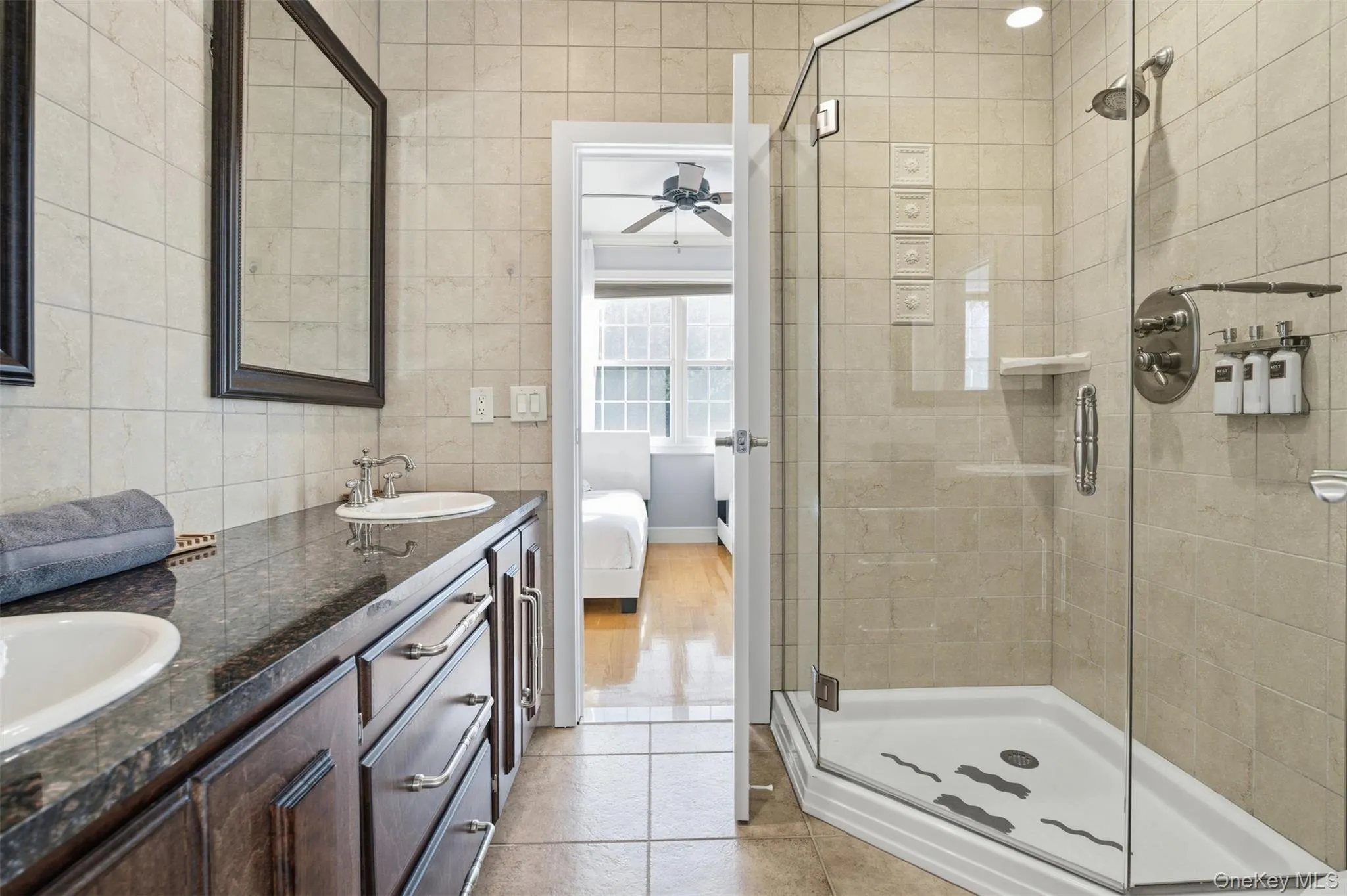 Bathroom featuring ensuite bath, double vanity, a shower stall, light tile patterned flooring, and a ceiling fan Bathroom featuring ensuite bath, double vanity, a shower stall, light tile patterned flooring, and a ceiling fan