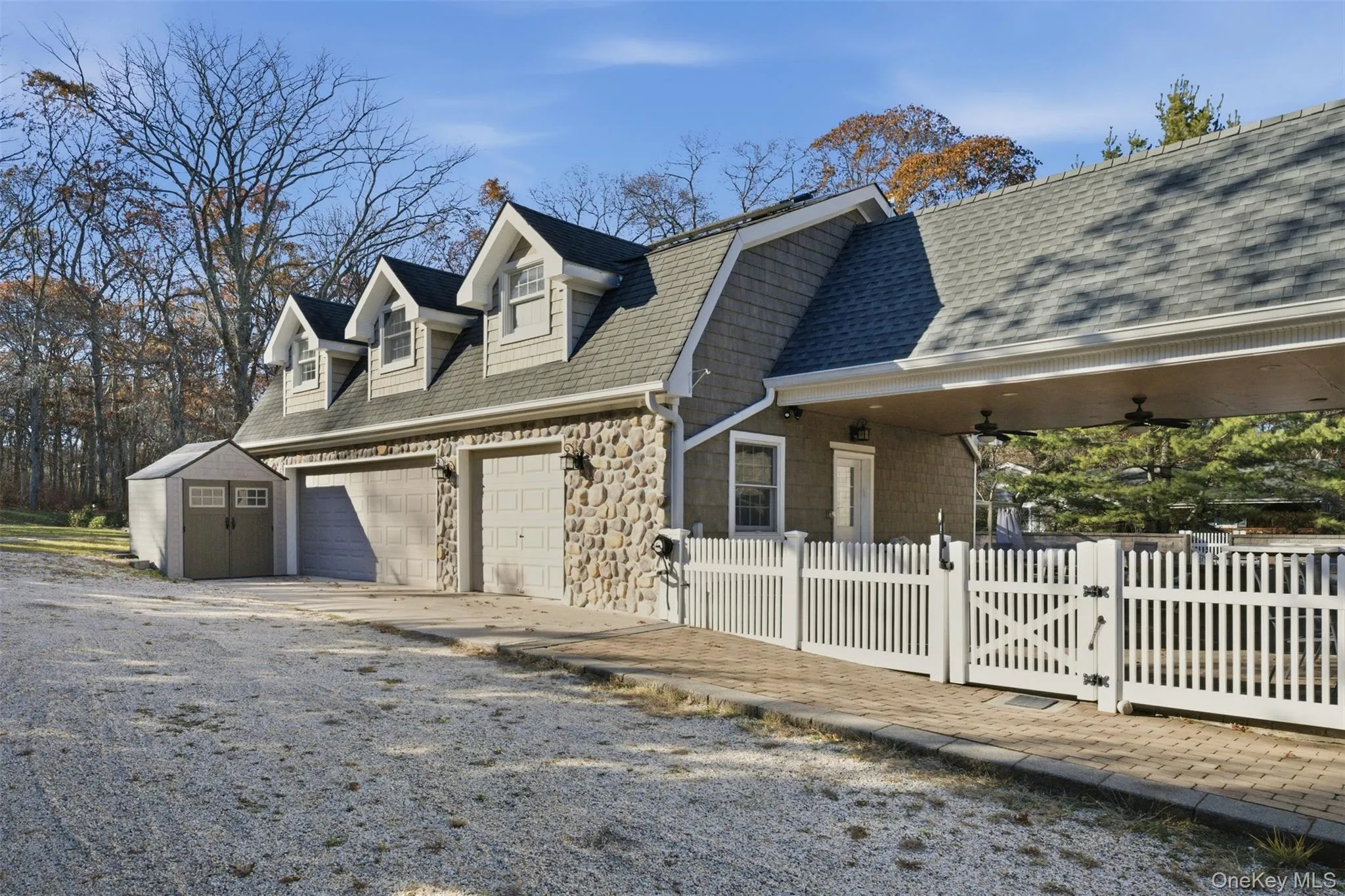 View of side of property featuring a gate, driveway, stone siding, a storage shed, and roof with shingles View of side of property featuring a gate, driveway, stone siding, a storage shed, and roof with shingles