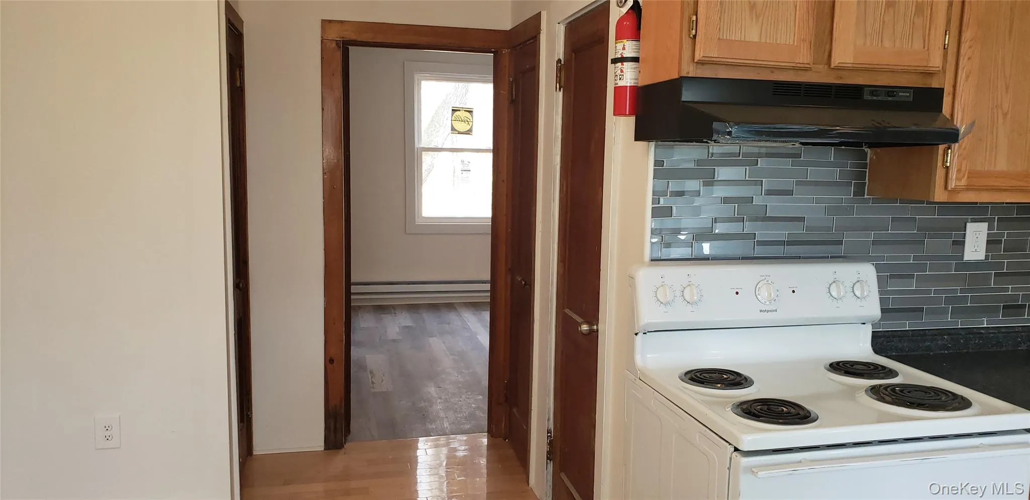 Kitchen with decorative backsplash, white electric range, under cabinet range hood, and light wood finished floors Kitchen with decorative backsplash, white electric range, under cabinet range hood, and light wood finished floors