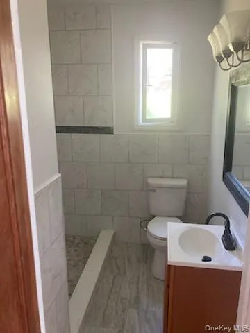 Full bathroom with tile walls, vanity, a wainscoted wall, and a walk in shower Full bathroom with tile walls, vanity, a wainscoted wall, and a walk in shower