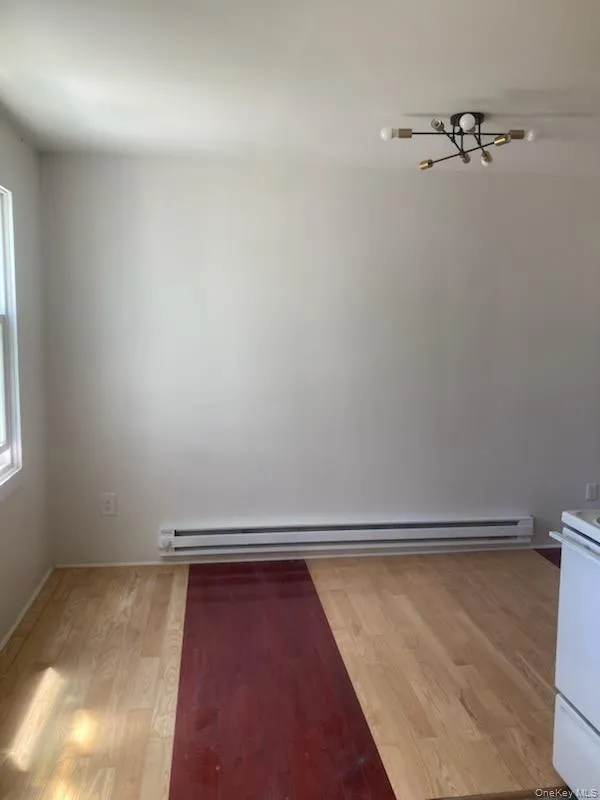 Unfurnished room featuring light wood-style floors, a baseboard radiator, and a chandelier Unfurnished room featuring light wood-style floors, a baseboard radiator, and a chandelier
