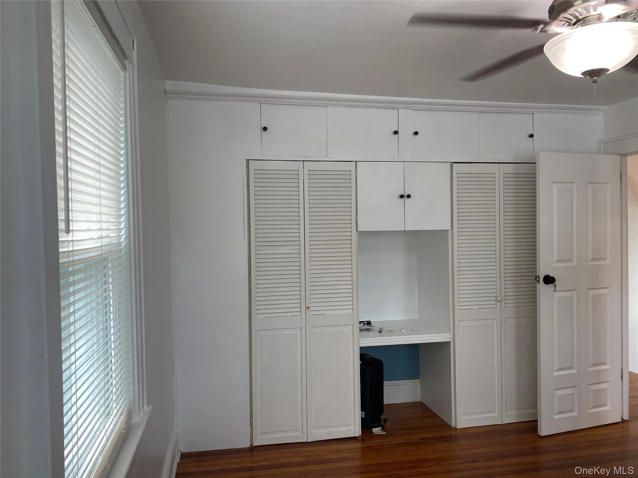 Unfurnished bedroom with multiple closets, built in study area, dark wood finished floors, and ceiling fan Unfurnished bedroom with multiple closets, built in study area, dark wood finished floors, and ceiling fan