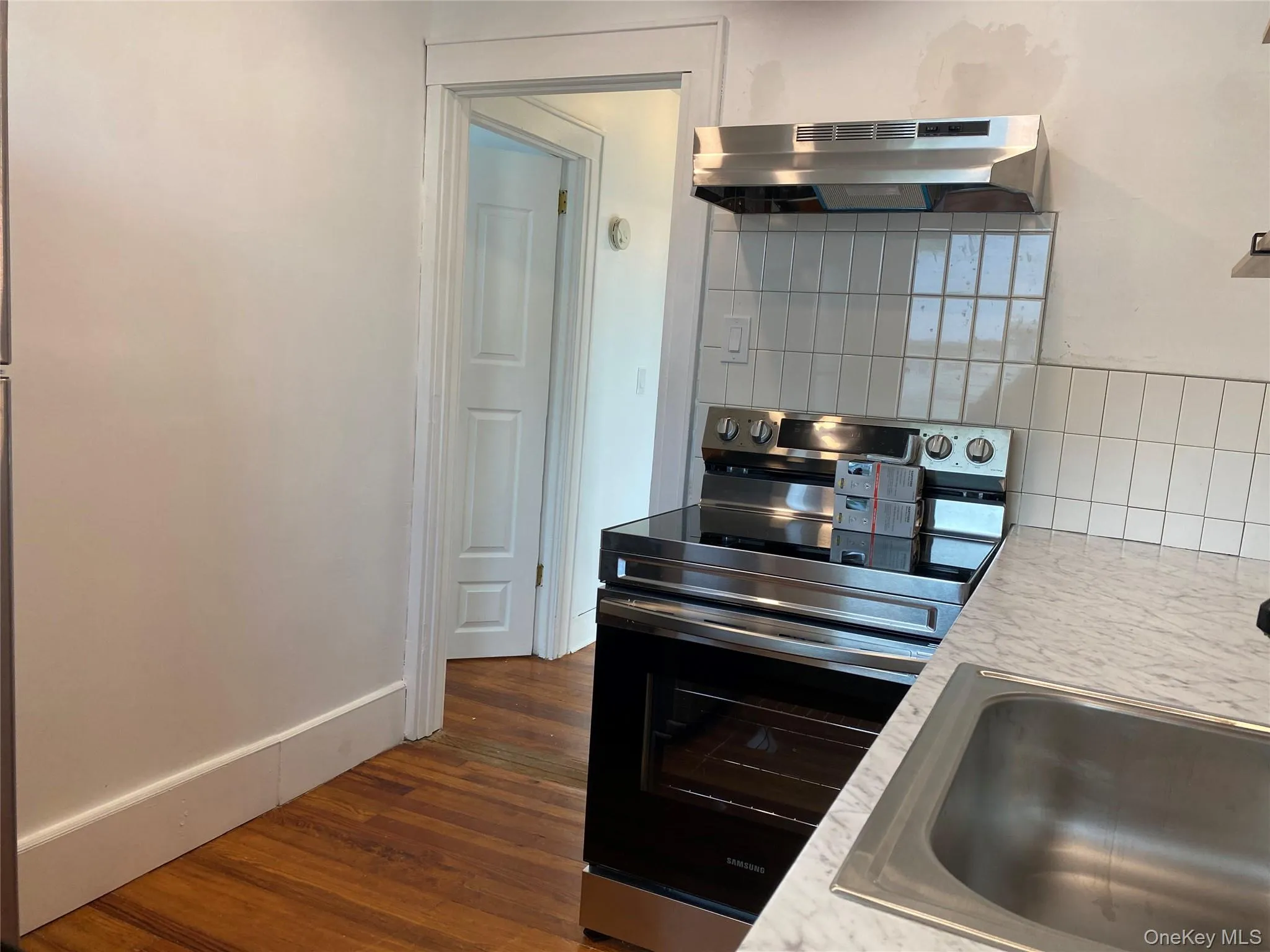 Kitchen with electric range, backsplash, light countertops, under cabinet range hood, and dark wood-type flooring Kitchen with electric range, backsplash, light countertops, under cabinet range hood, and dark wood-type flooring
