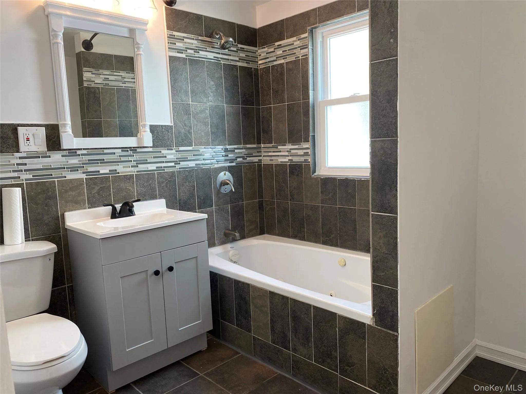 Bathroom featuring dark tile patterned flooring, vanity, and tile walls Bathroom featuring dark tile patterned flooring, vanity, and tile walls