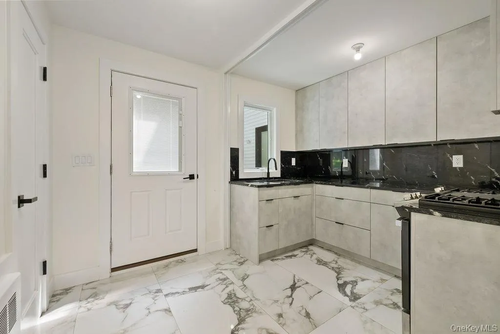 Kitchen with dark stone counters, light marble finish flooring, range with gas cooktop, backsplash, and modern cabinets Kitchen with dark stone counters, light marble finish flooring, range with gas cooktop, backsplash, and modern cabinets