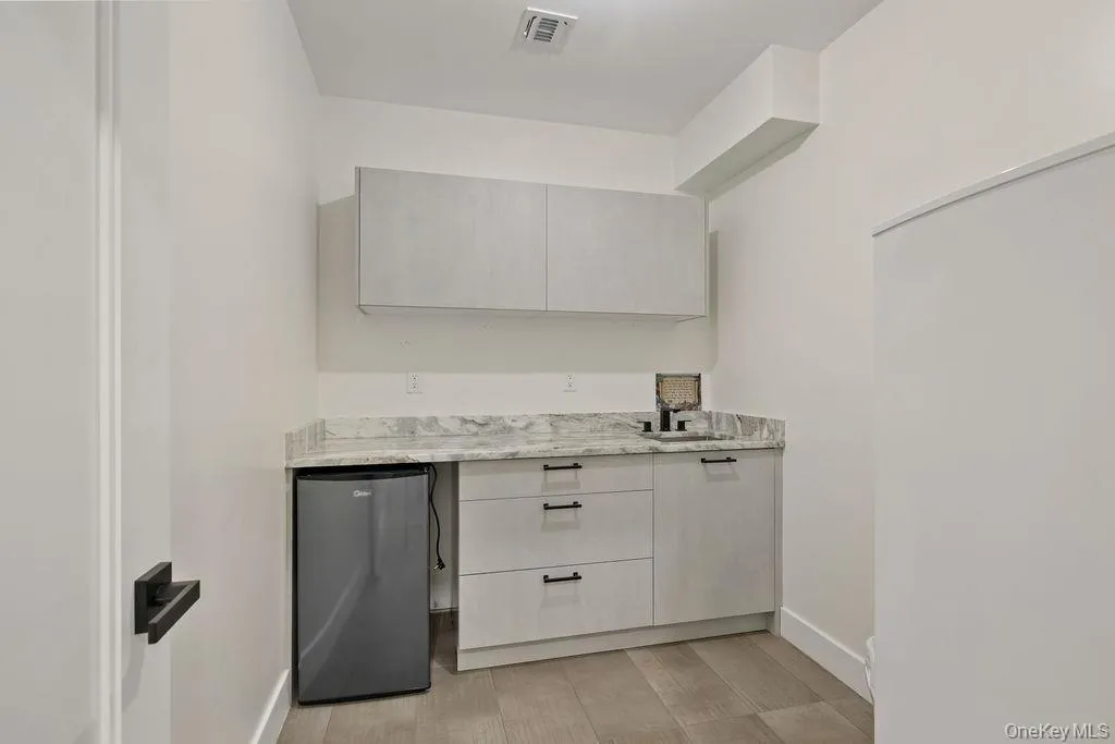 Bar featuring stainless steel refrigerator, light stone countertops, and light wood finished floors Bar featuring stainless steel refrigerator, light stone countertops, and light wood finished floors