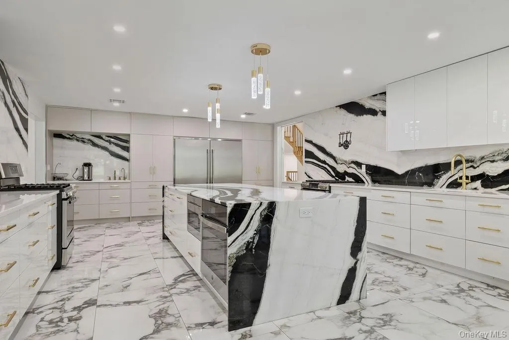 Kitchen with modern cabinets, hanging light fixtures, light stone counters, stainless steel appliances, and a center island Kitchen with modern cabinets, hanging light fixtures, light stone counters, stainless steel appliances, and a center island