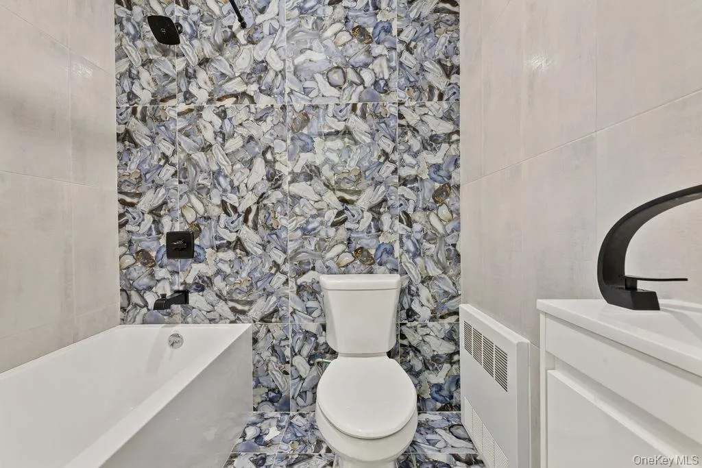Full bath with a bath, vanity, tile walls, and radiator heating unit Full bath with a bath, vanity, tile walls, and radiator heating unit