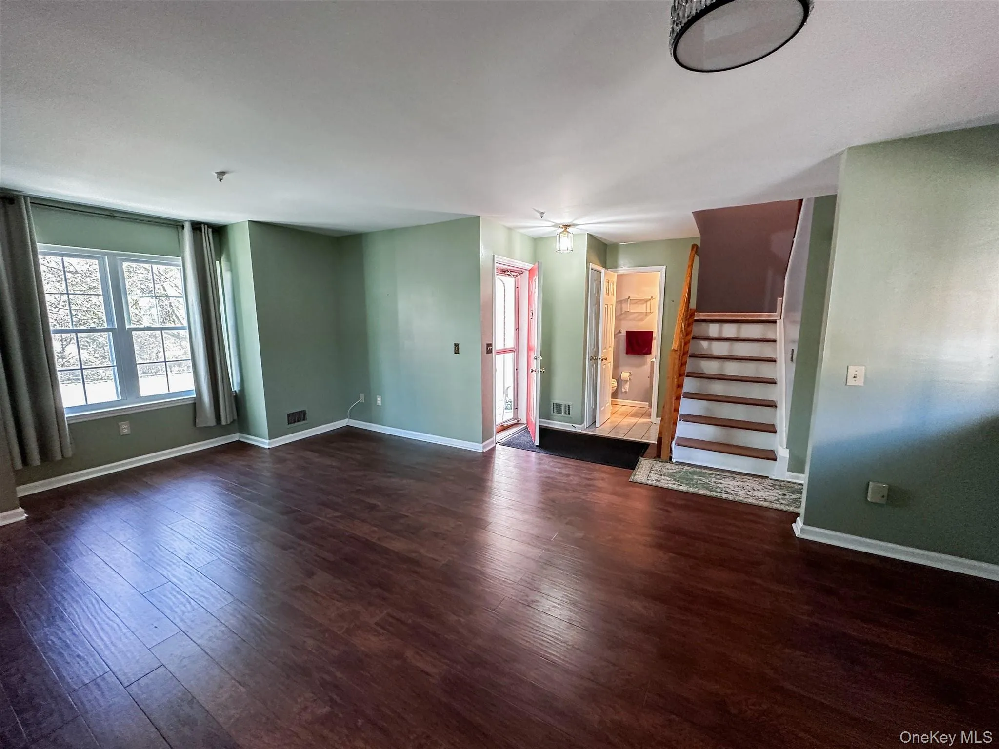 Unfurnished living room featuring stairway and dark wood-style floors Unfurnished living room featuring stairway and dark wood-style floors
