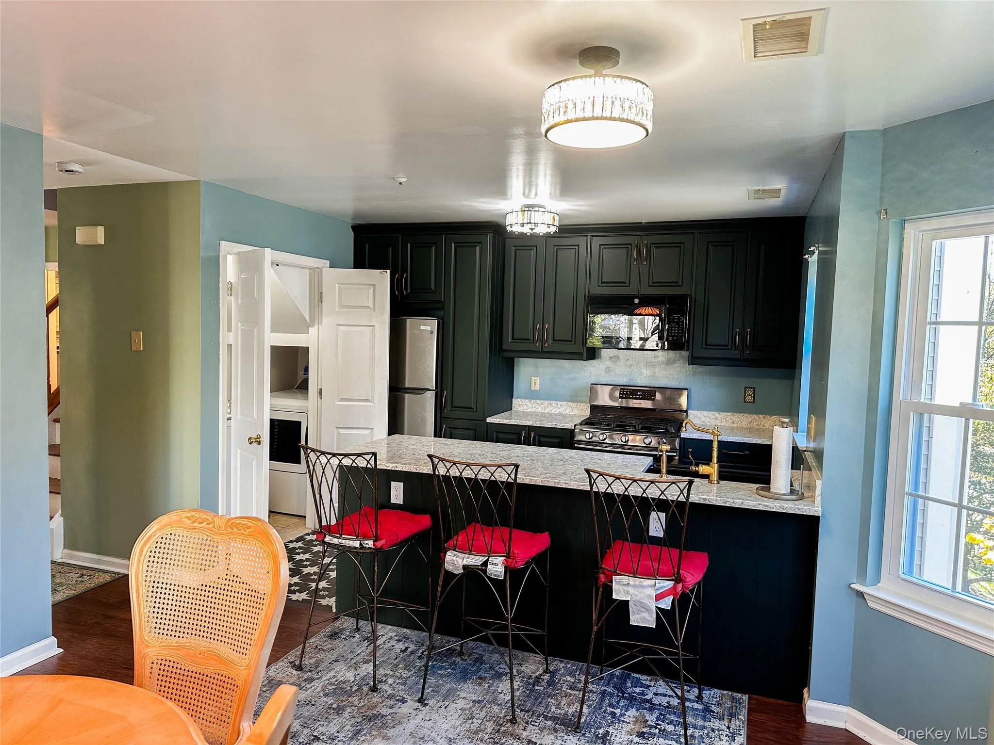 Kitchen with a peninsula, stainless steel appliances, a kitchen bar, light stone counters, and dark wood-style floors Kitchen with a peninsula, stainless steel appliances, a kitchen bar, light stone counters, and dark wood-style floors