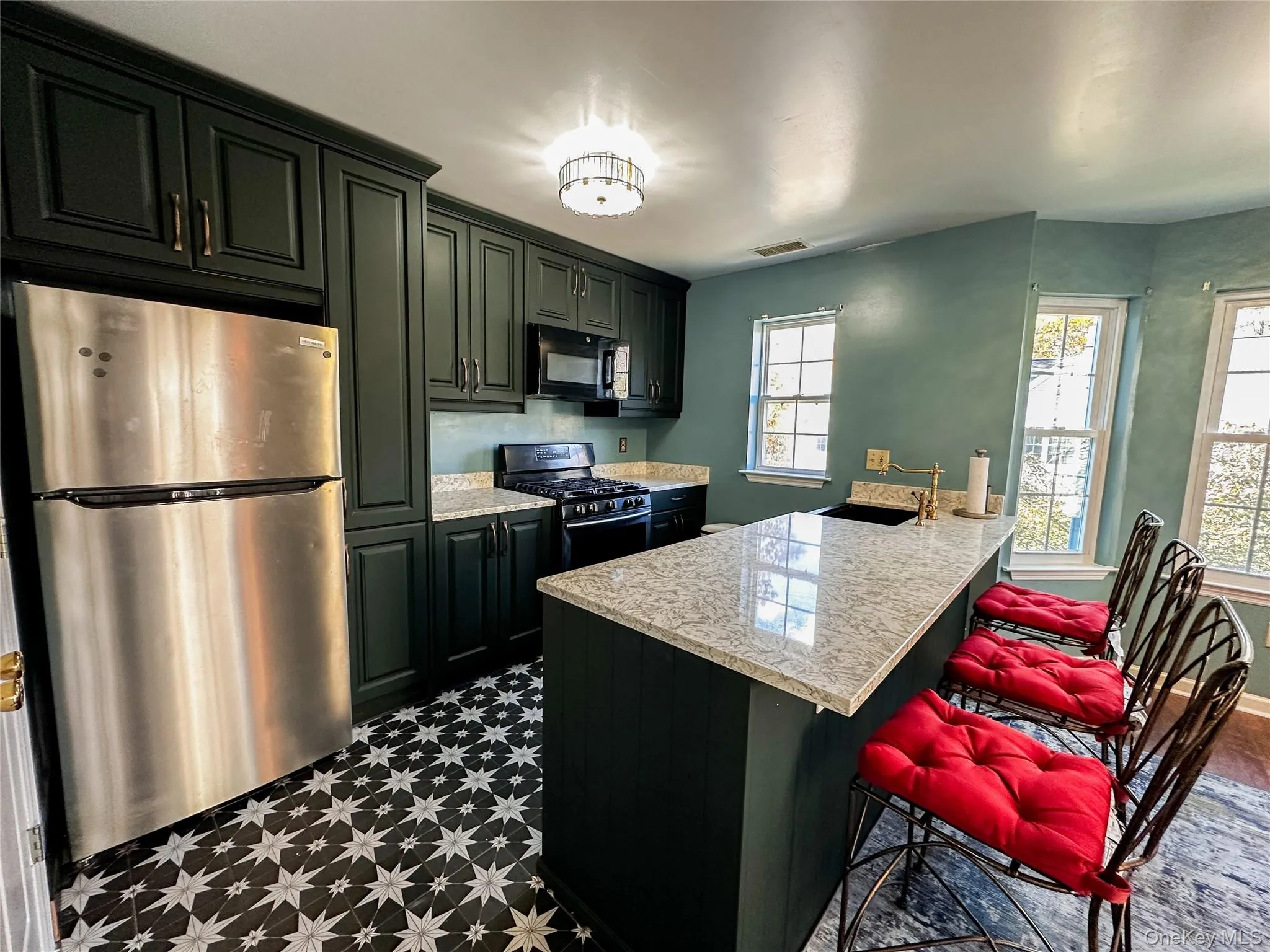 Kitchen with black appliances, dark flooring, a breakfast bar, a peninsula, and light stone countertops Kitchen with black appliances, dark flooring, a breakfast bar, a peninsula, and light stone countertops
