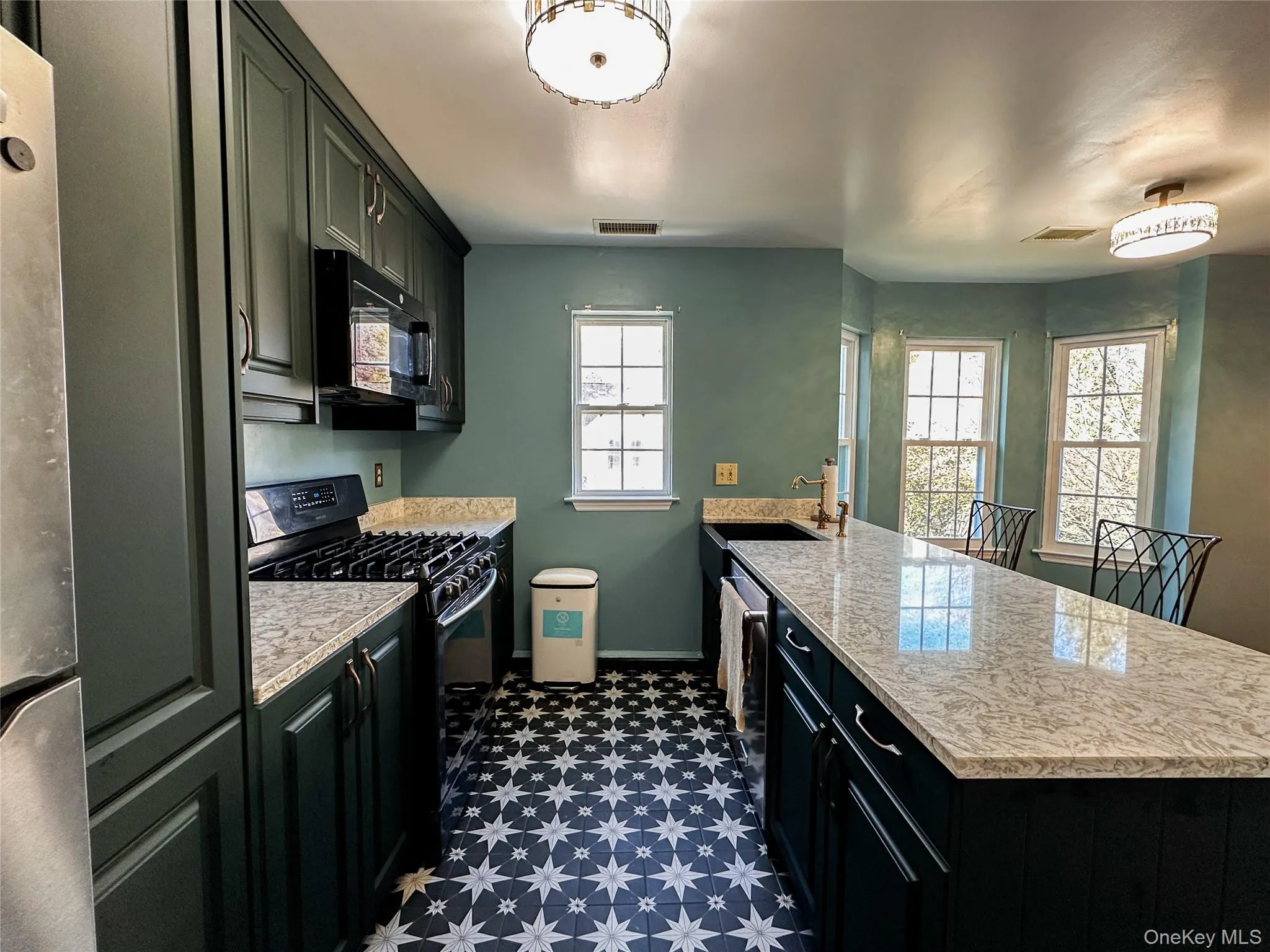 Kitchen with dark cabinetry, black appliances, a peninsula, dark floors, and light stone countertops Kitchen with dark cabinetry, black appliances, a peninsula, dark floors, and light stone countertops
