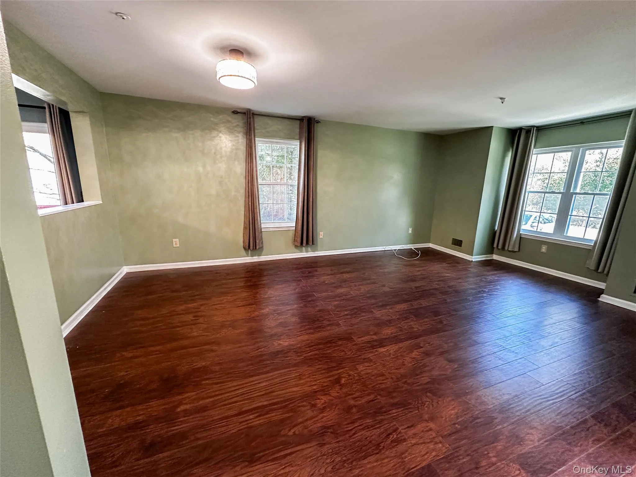 Empty room with dark wood-style flooring and baseboards Empty room with dark wood-style flooring and baseboards